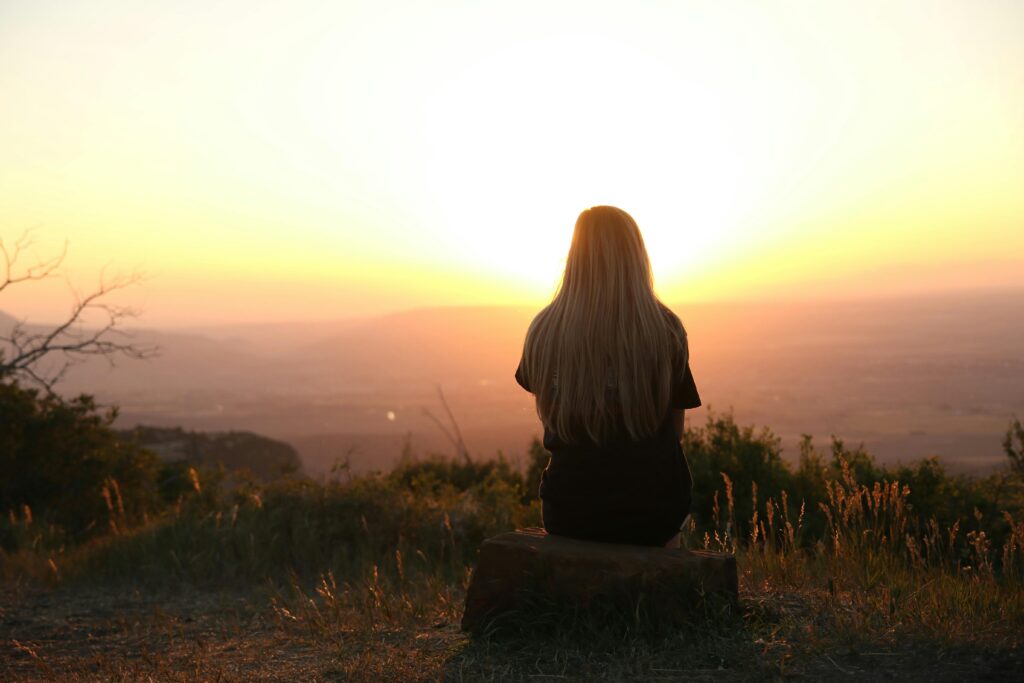 Woman sitting on a hill looking out at the sunset