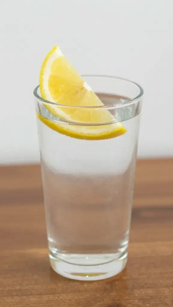 Closeup of a single glass of water with lemon wedge on a wooden bedside table