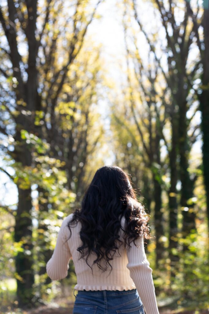 a woman facing away from the camera walking through a forest