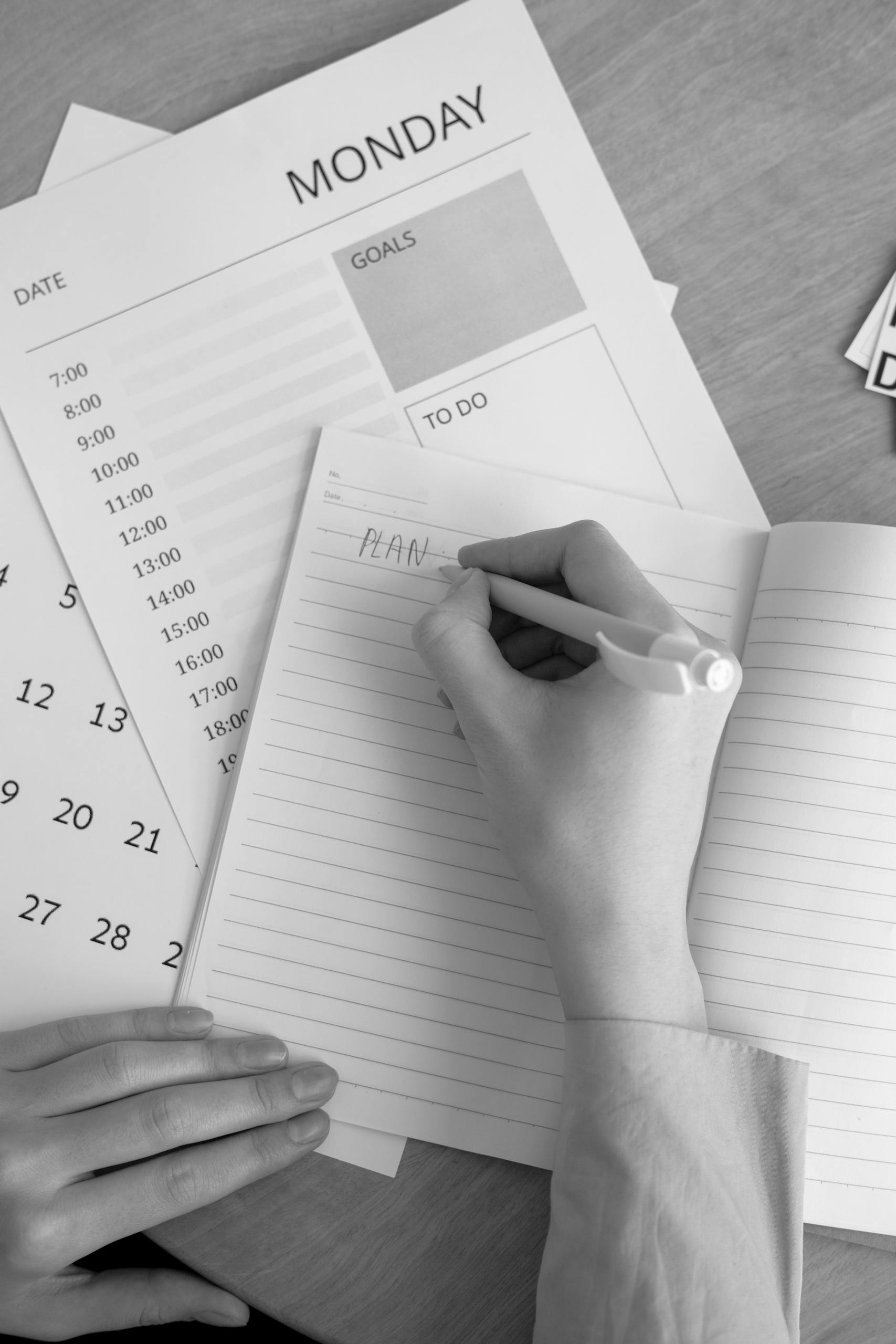 A monochrome image of a person planning their week with a notebook, calendar, and goals list.
