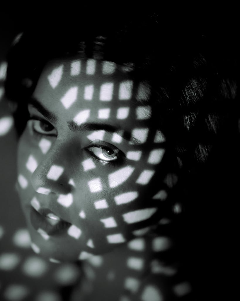 Dramatic portrait of a person in black and white with artistic light patterns creating a moody atmosphere.