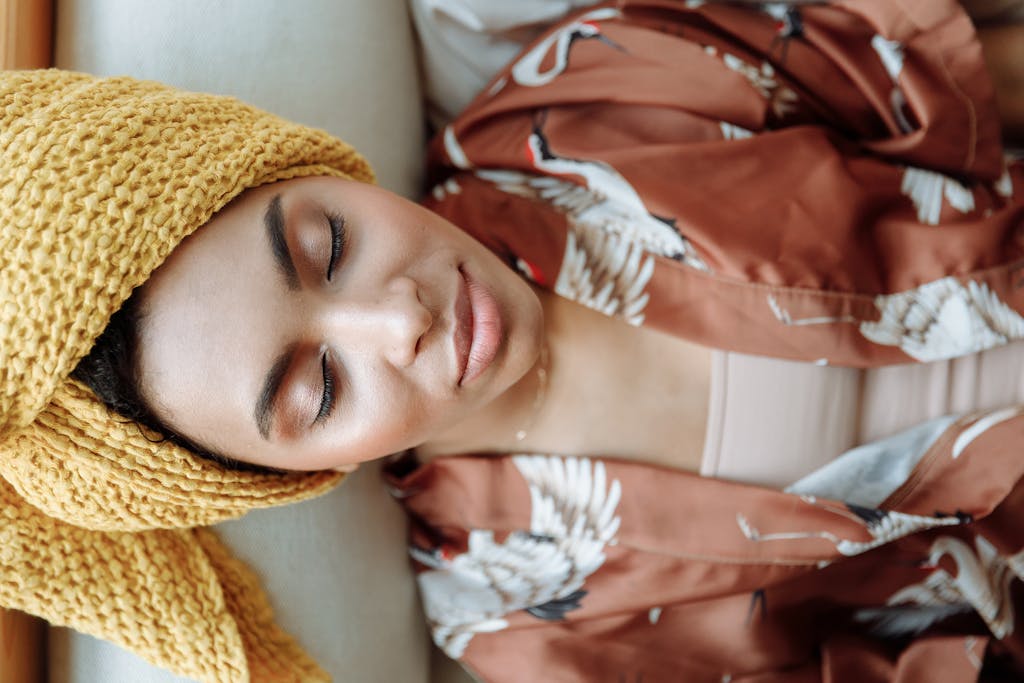 Peaceful woman with closed eyes, wearing a towel and patterned robe indoors.