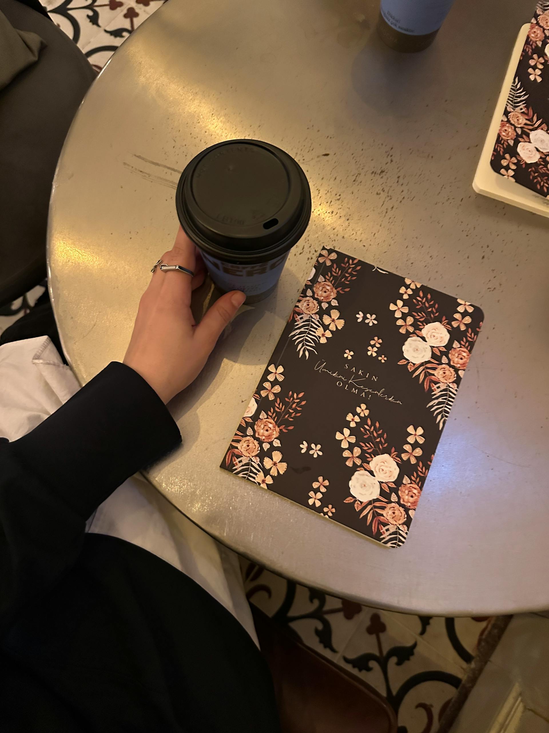 A cozy scene with a coffee cup and floral notebook on a café table writing simple morning journal prompts