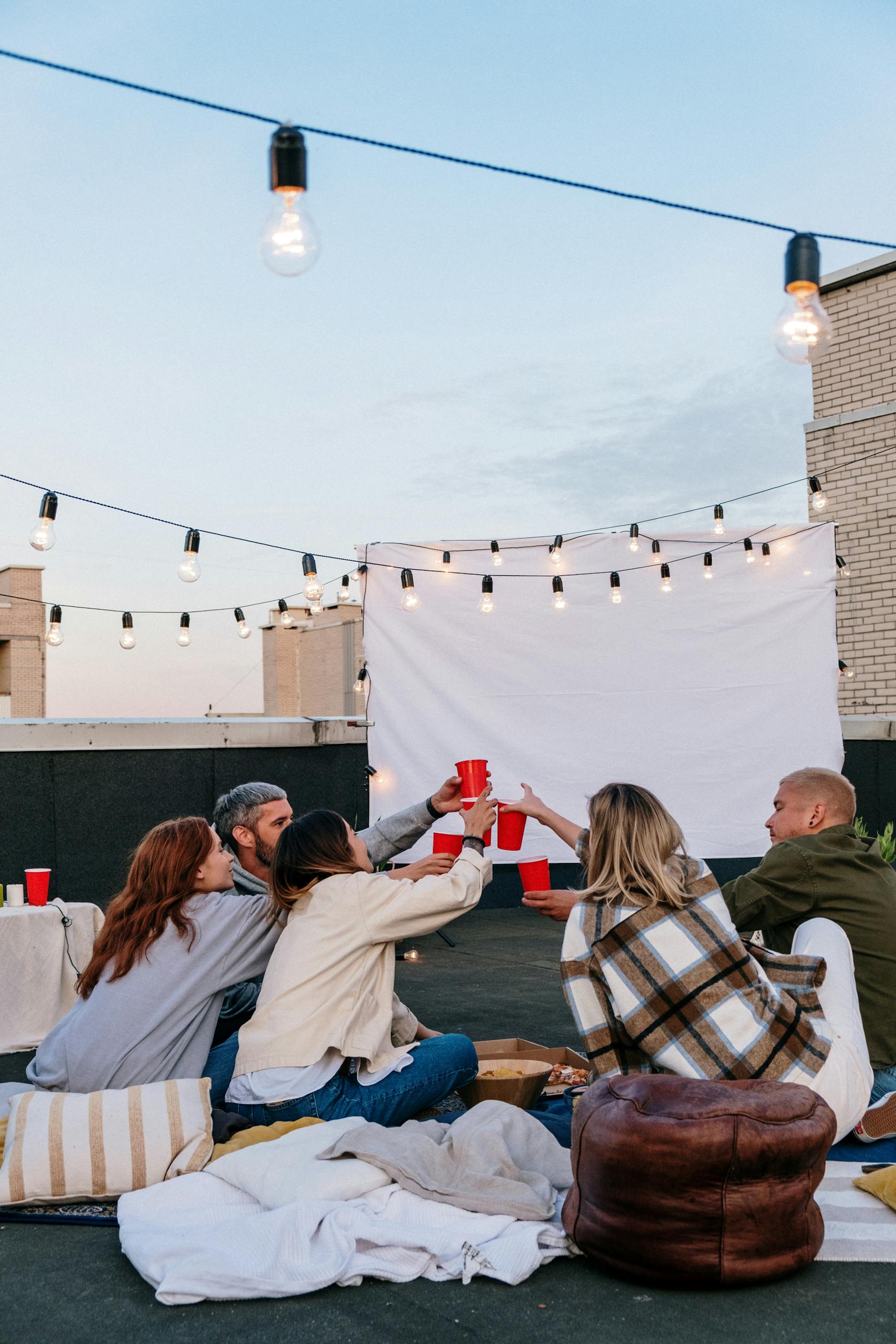 A group of friends enjoying a rooftop party with drinks under string lights.
