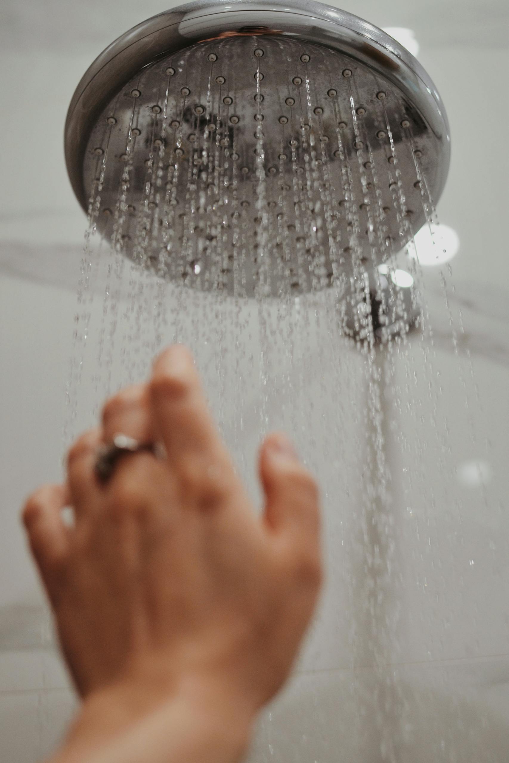 A hand reaches toward a shower head, capturing water droplets in motion for the everything shower steps.