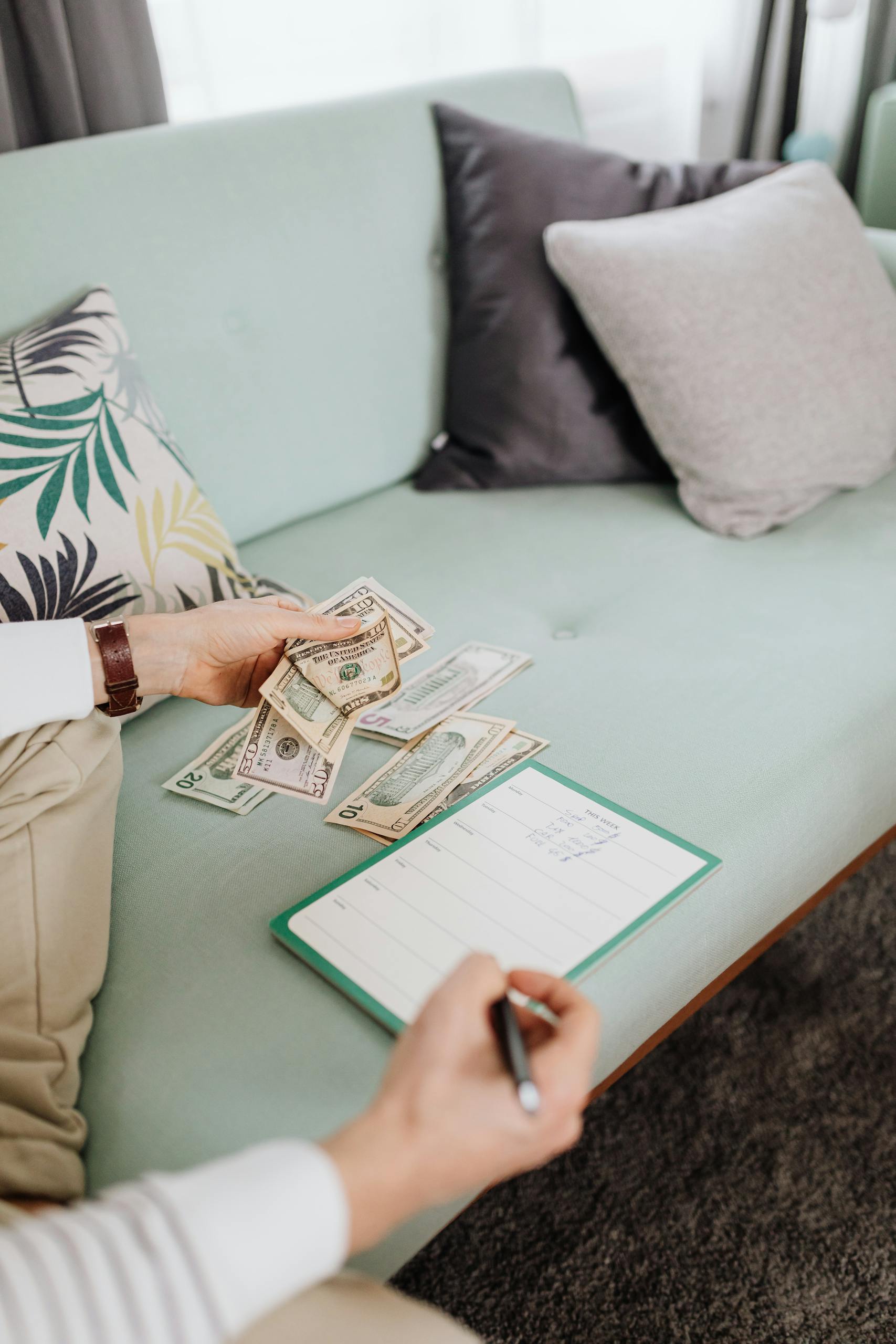 A person counting cash on a couch with a notebook, representing personal finance management.