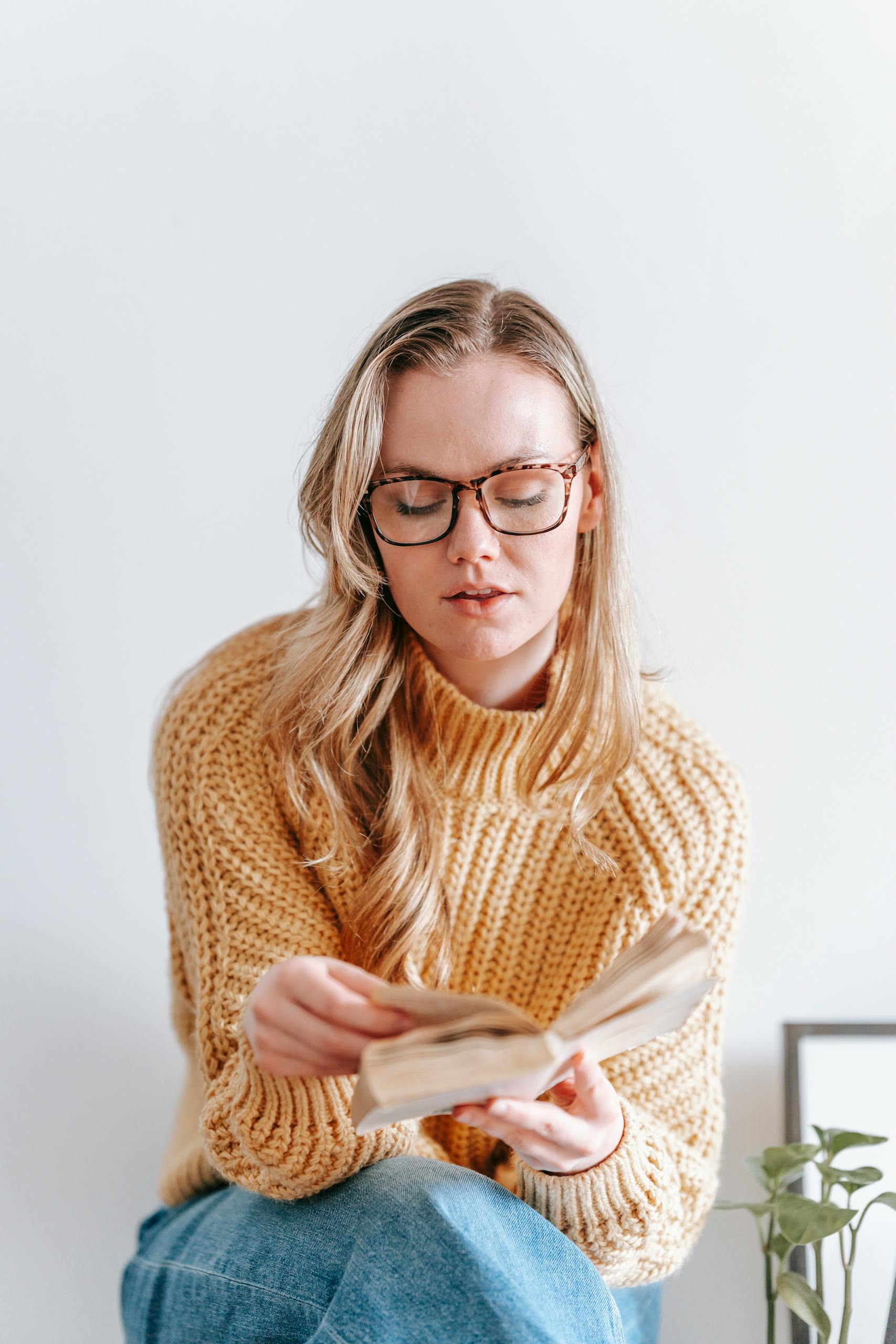 A woman in a knitted sweater enjoys reading a book indoors.