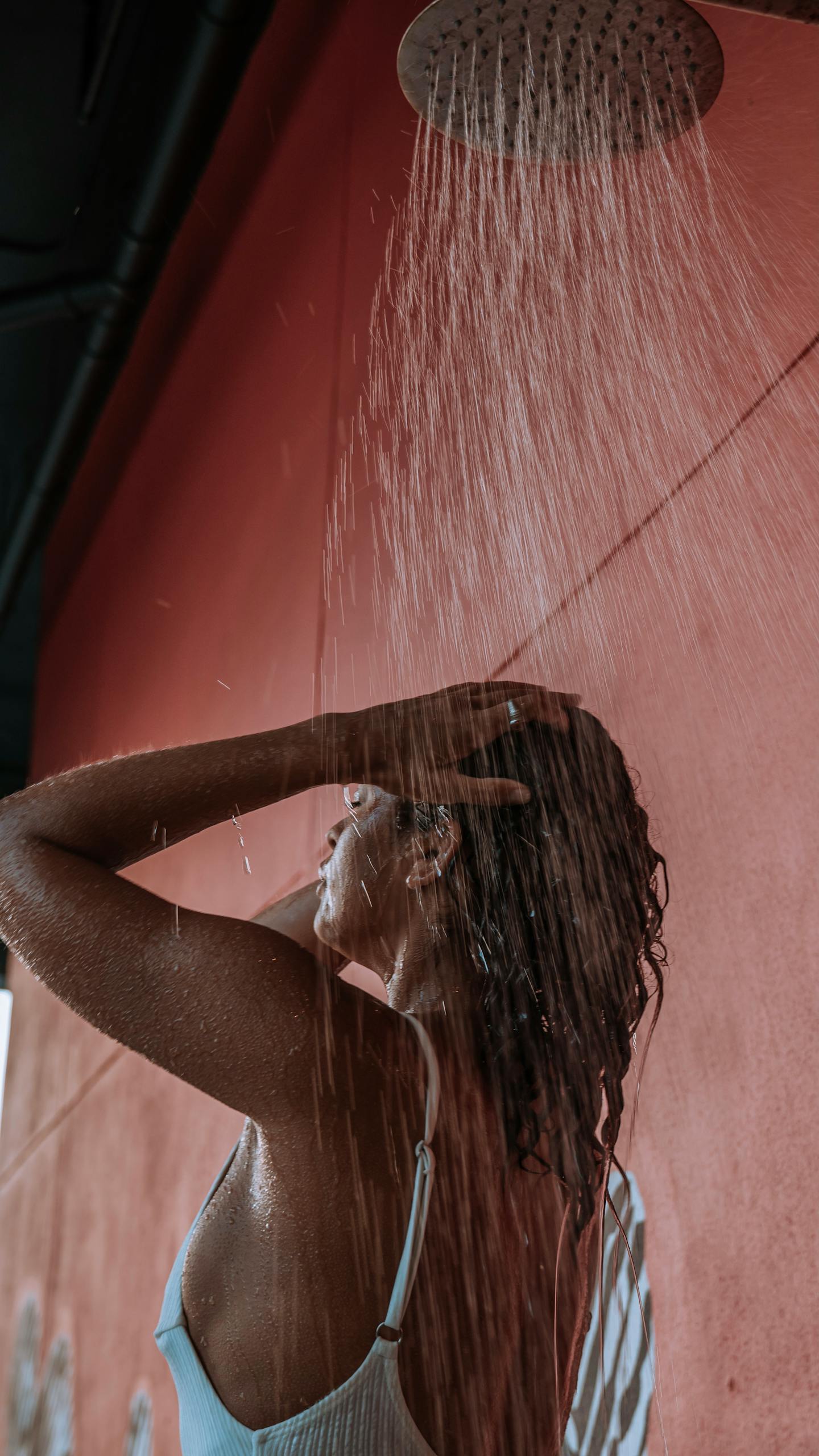 A woman in a swimsuit takes a refreshing outdoor shower, hands on head with water streaming down doing the everything shower checklist.