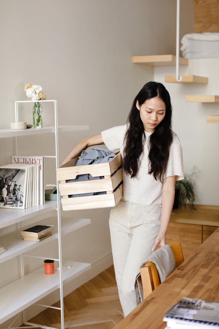 Asian woman organizing laundry in a modern home interior, emphasizing cleanliness and minimalism.