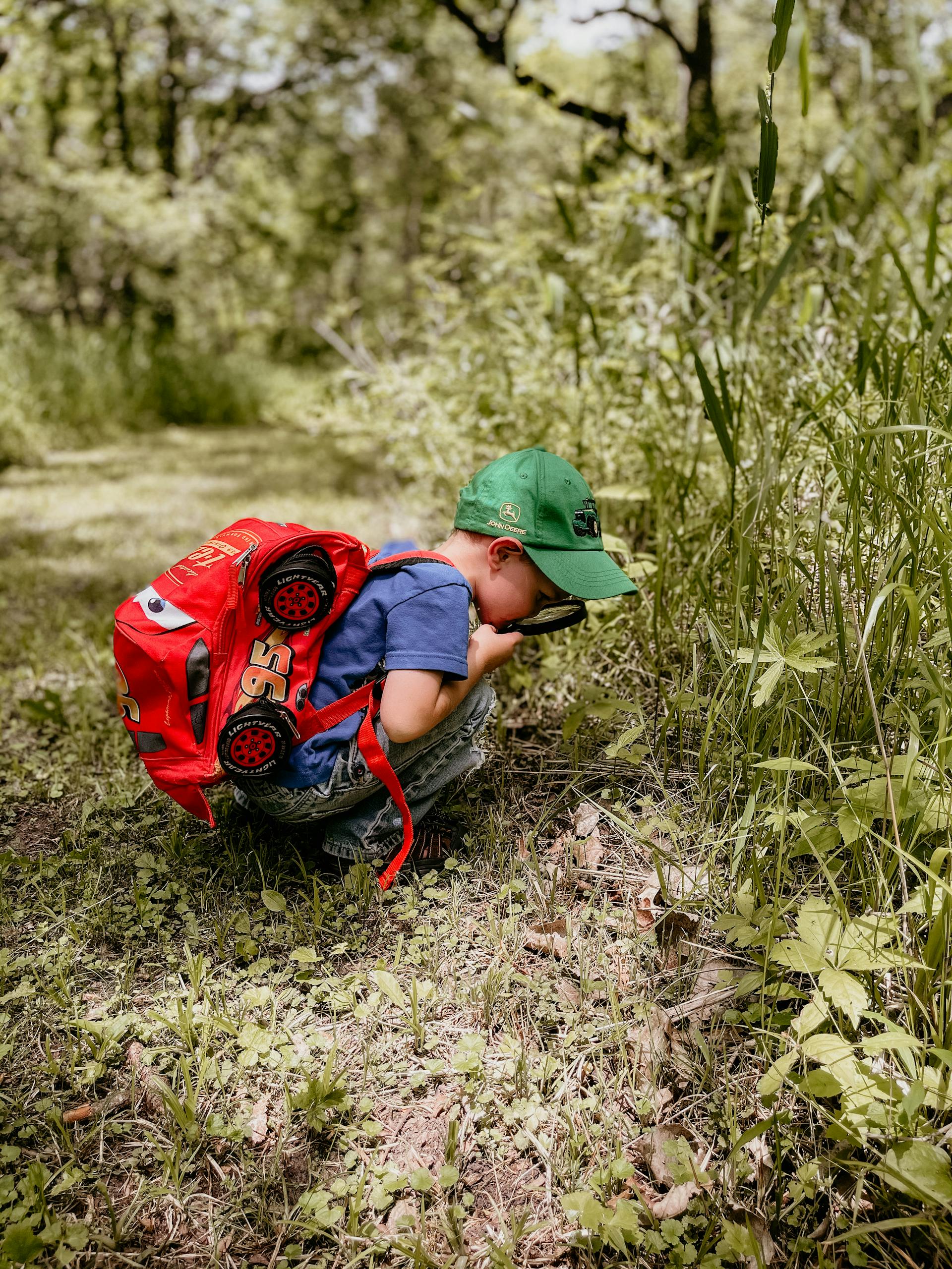 Child exploring nature with a magnifying glass, wearing a vibrant backpack.