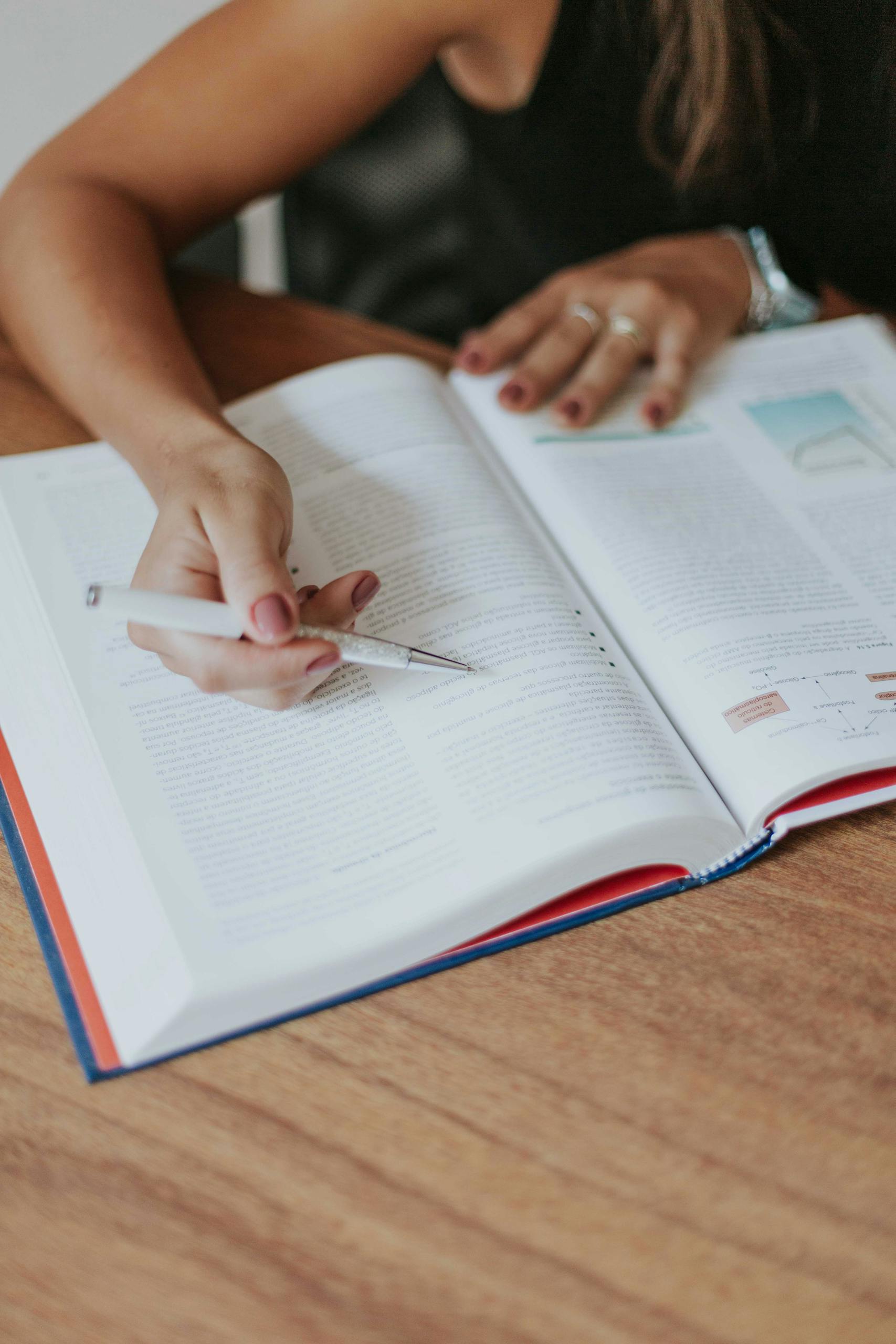 Close-up of an adult woman studying with a pen in hand, reading a textbook at a wooden table. learning one of the life areas for goal setting