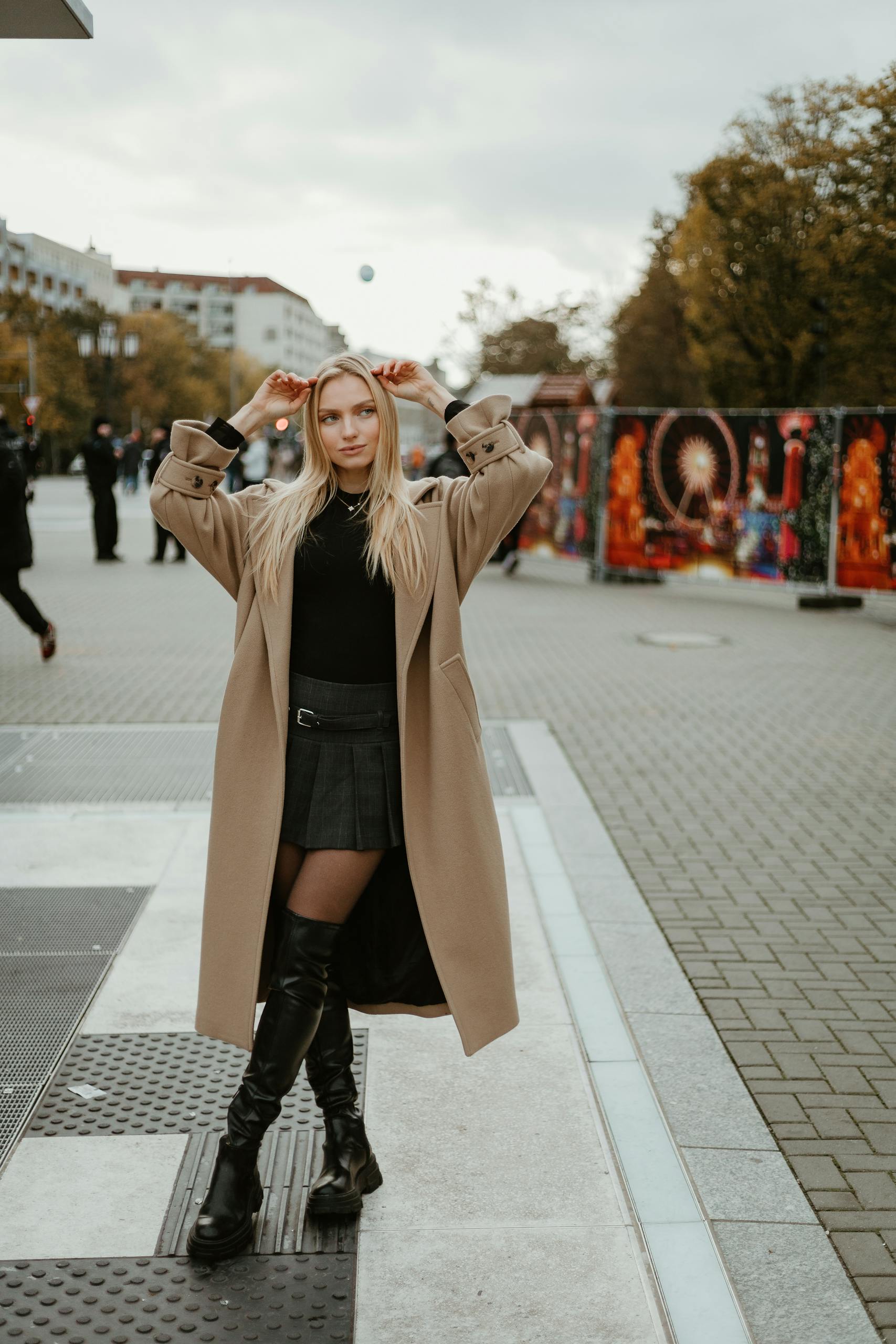 Elegant woman poses in city street, showcasing fall fashion with coat and boots.