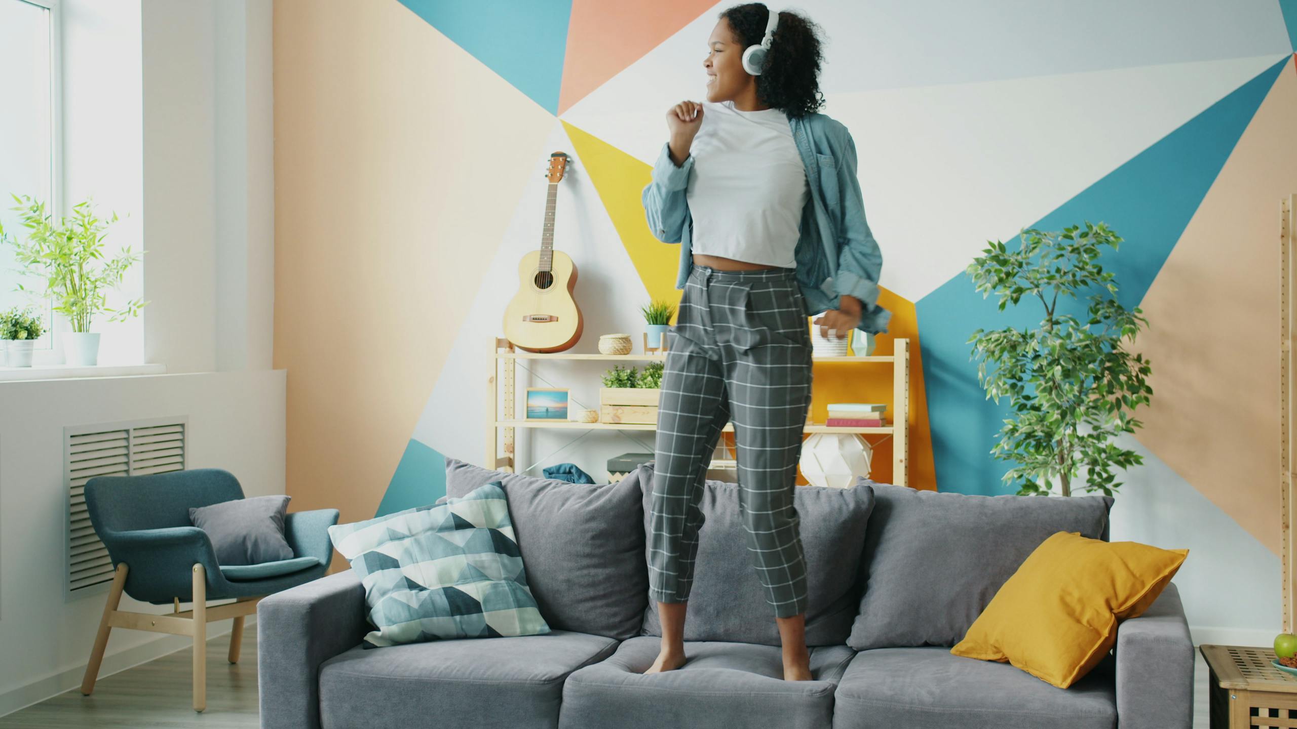 Energetic woman enjoying music, dancing joyfully on a comfortable couch.