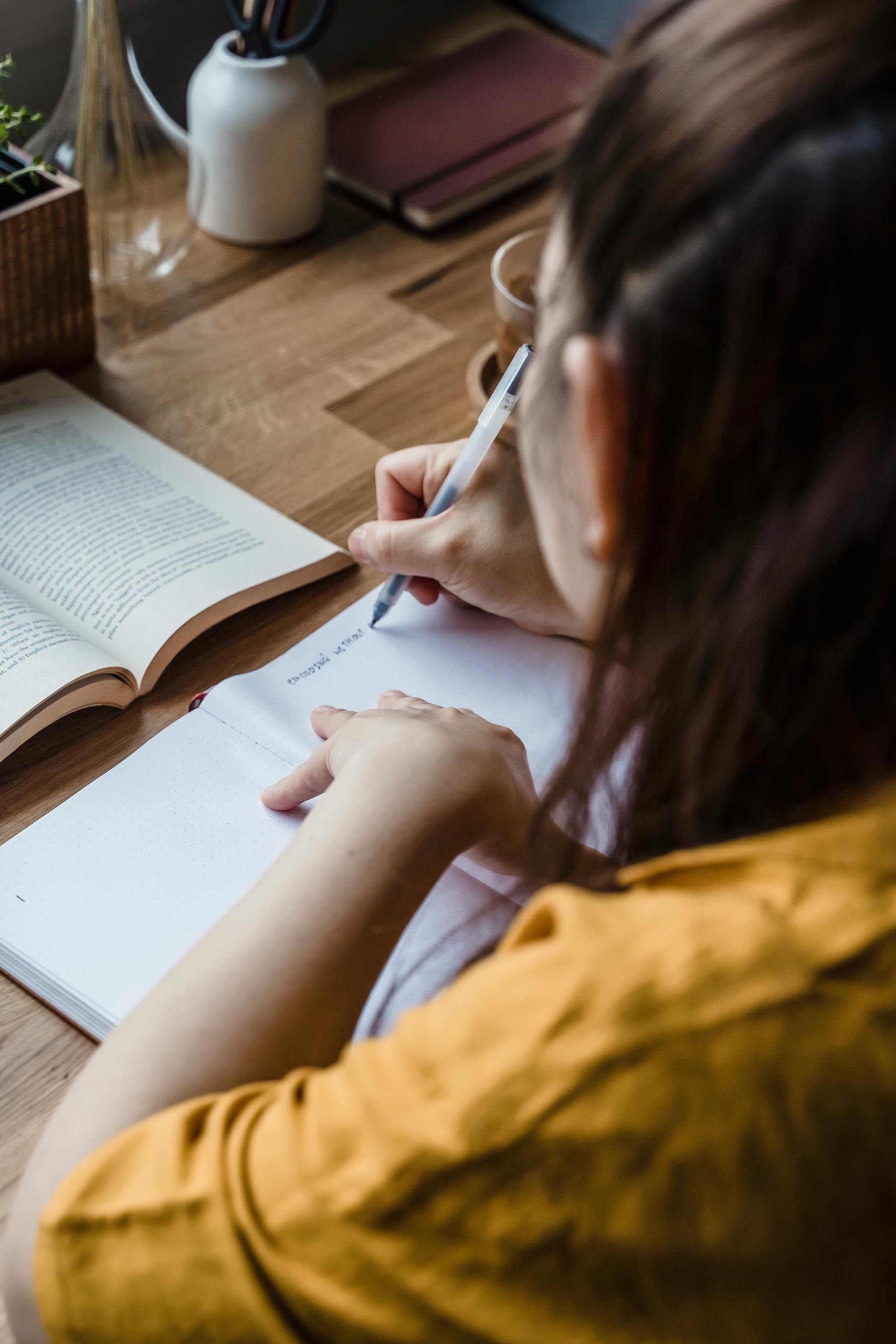 Focused woman writing in a notebook at a wooden desk, creating a serene and introspective scene.