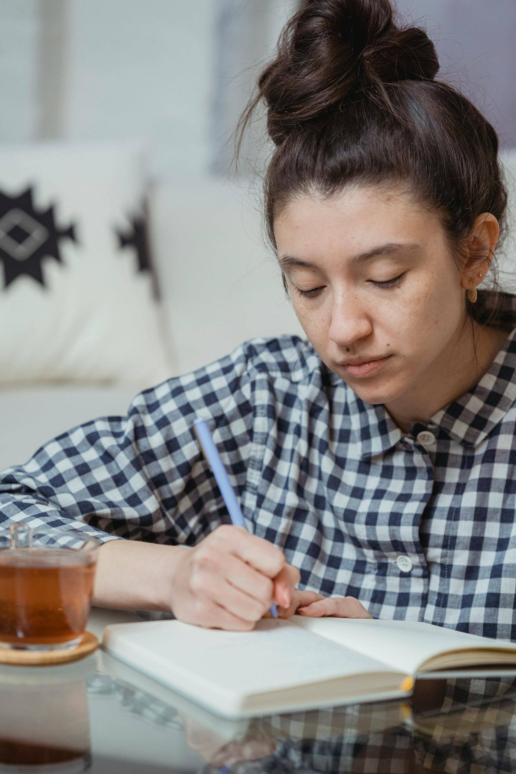 Focused young woman writing in a notebook at home with a cup of tea nearby.