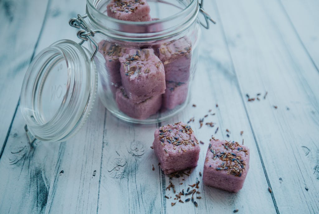 From above of fragrant square lavender bath bombs in transparent glass jar placed on white wooden table