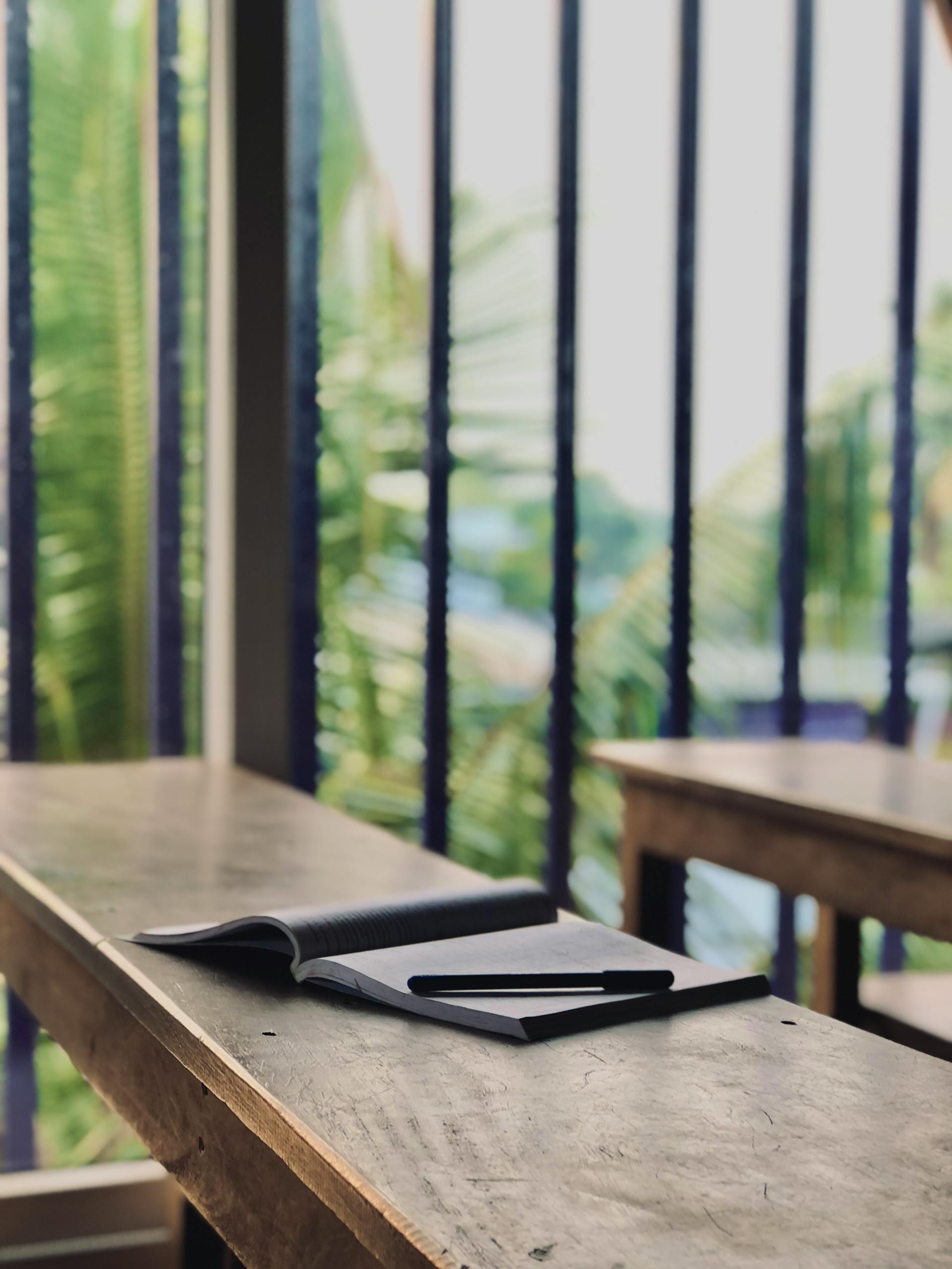 Open notebook with pen on rustic table overlooking lush green palms.
