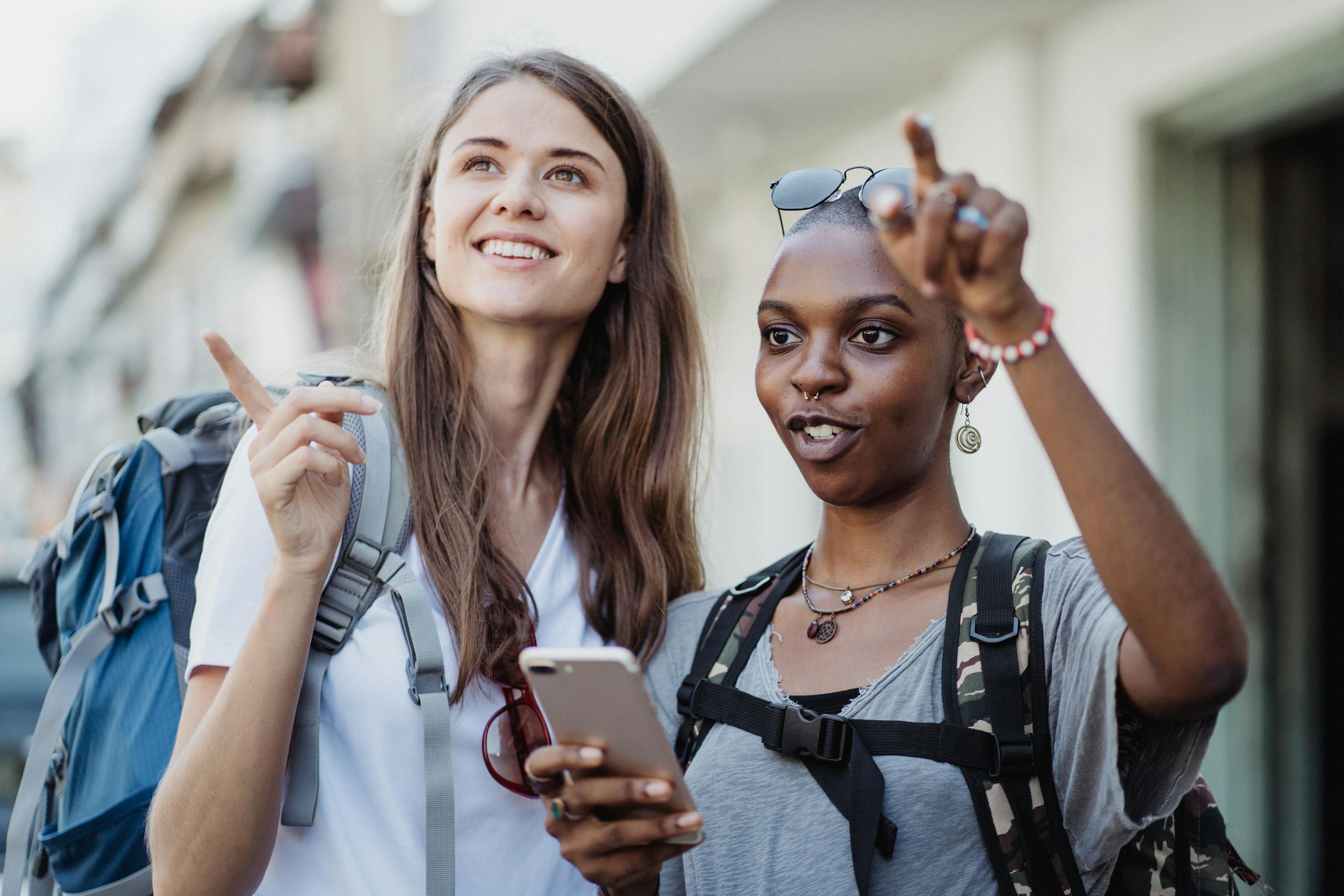 Two smiling women with backpacks navigating a city using a smartphone, embracing adventure and travel.