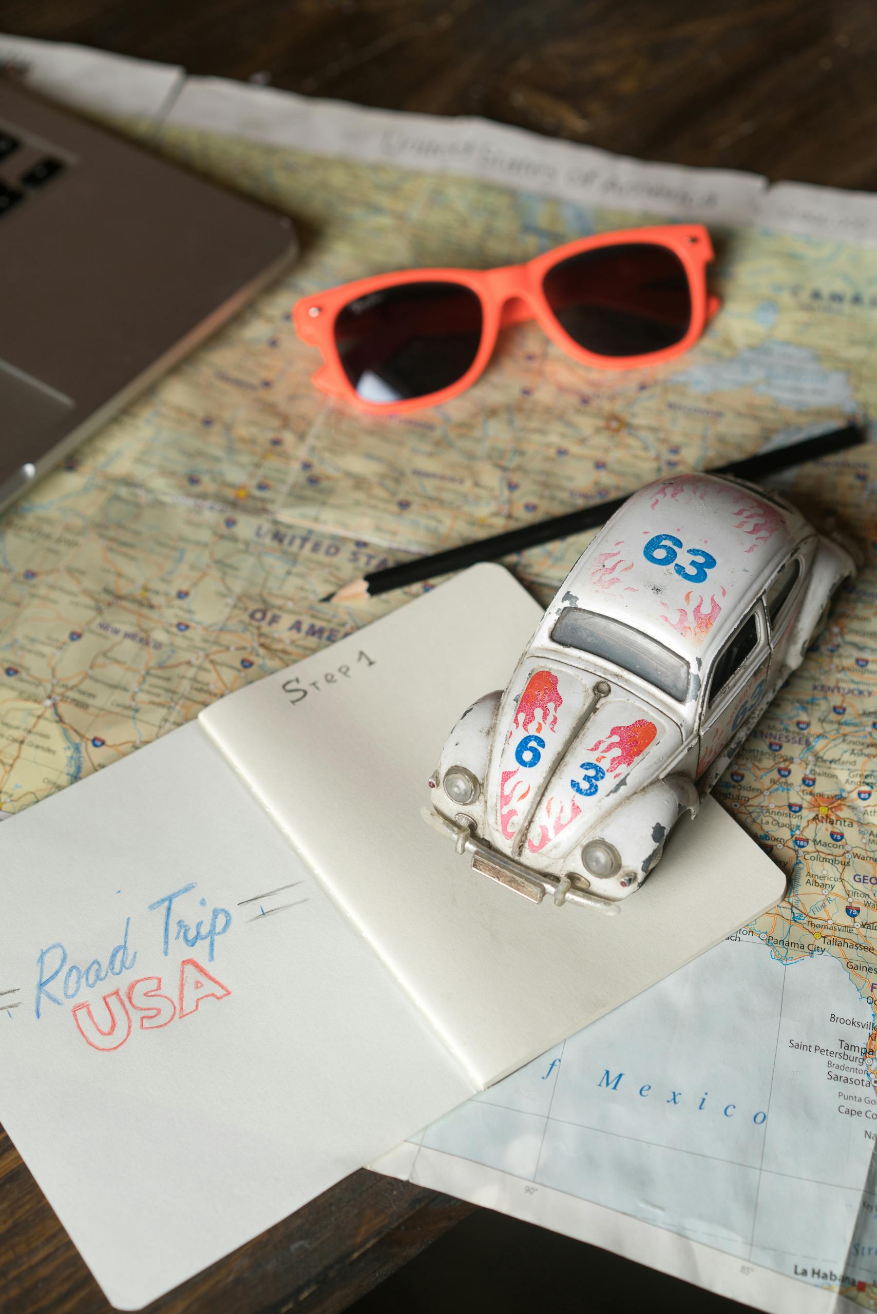 Vintage travel vibe with toy car, map, notebook, sunglasses, and pencil.