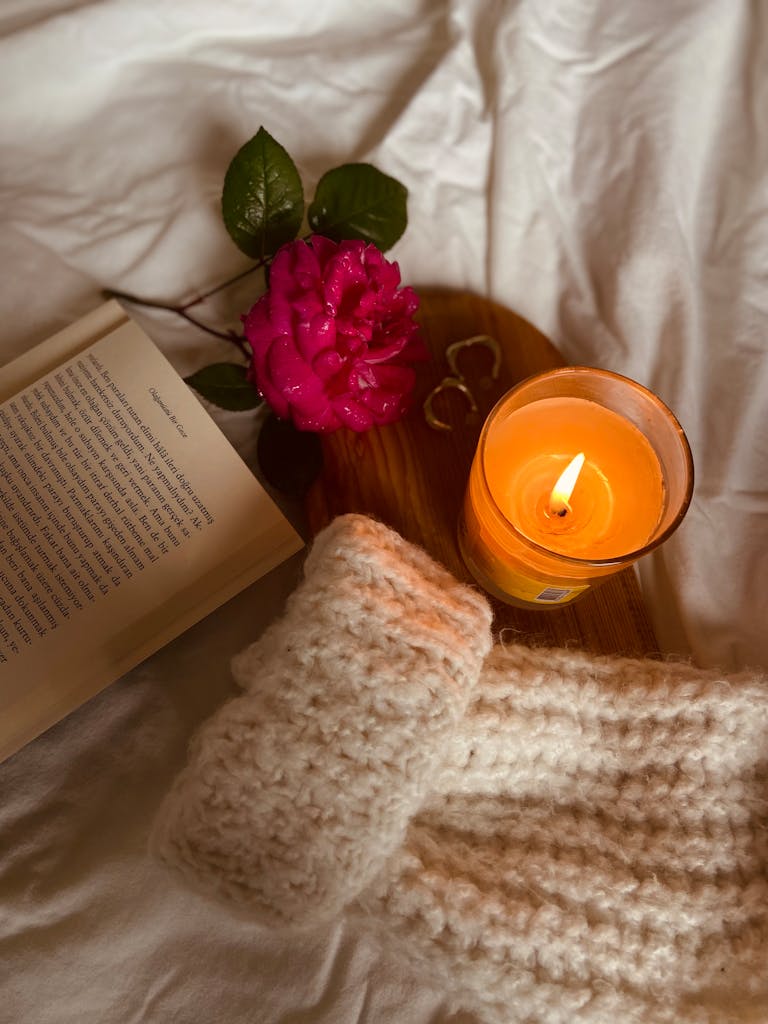 Warm autumn scene with a candle, book, rose, and knitted scarf, perfect for cozy nights.