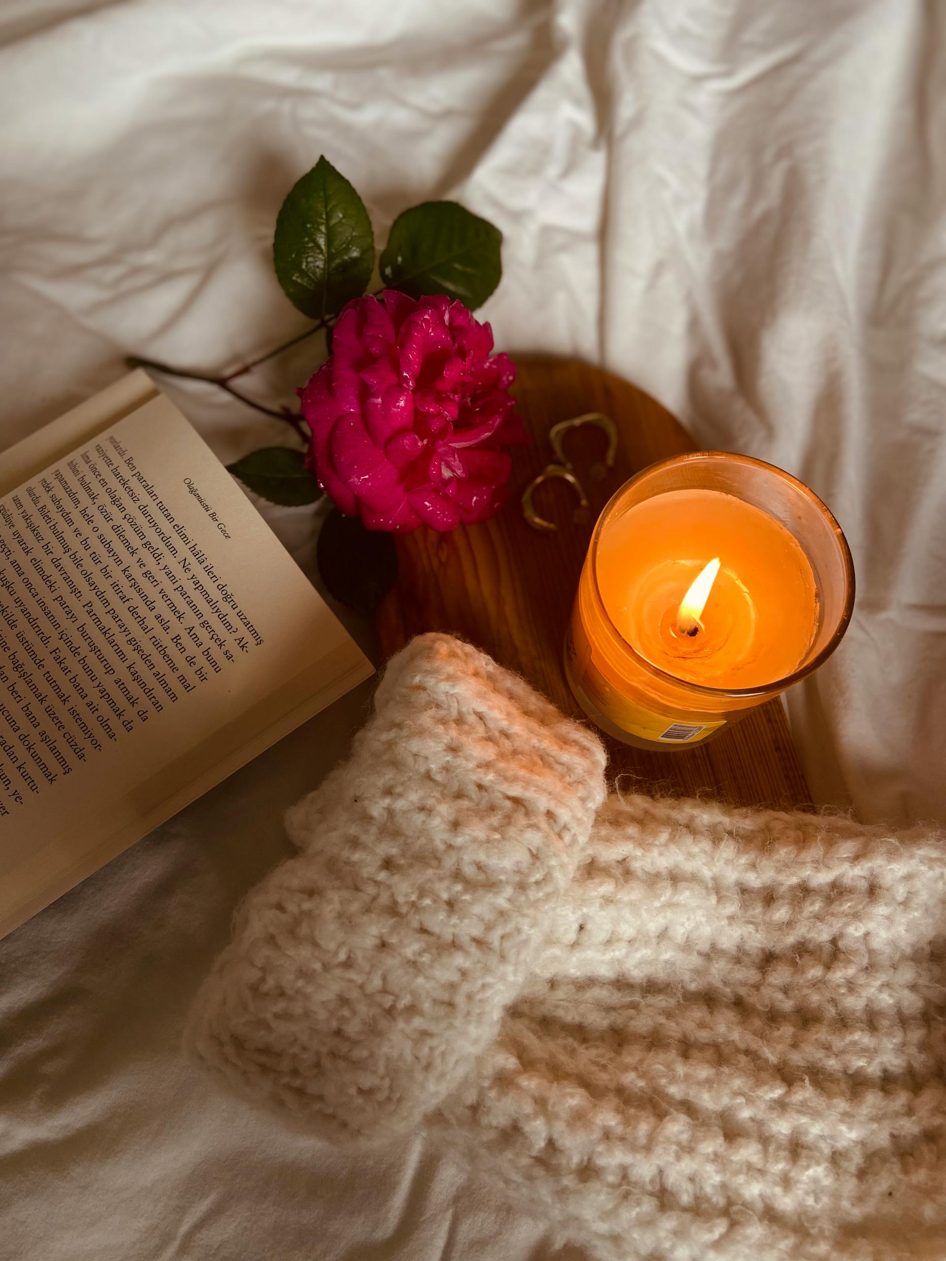 Warm autumn scene with a candle, book, rose, and knitted scarf, perfect for cozy nights.