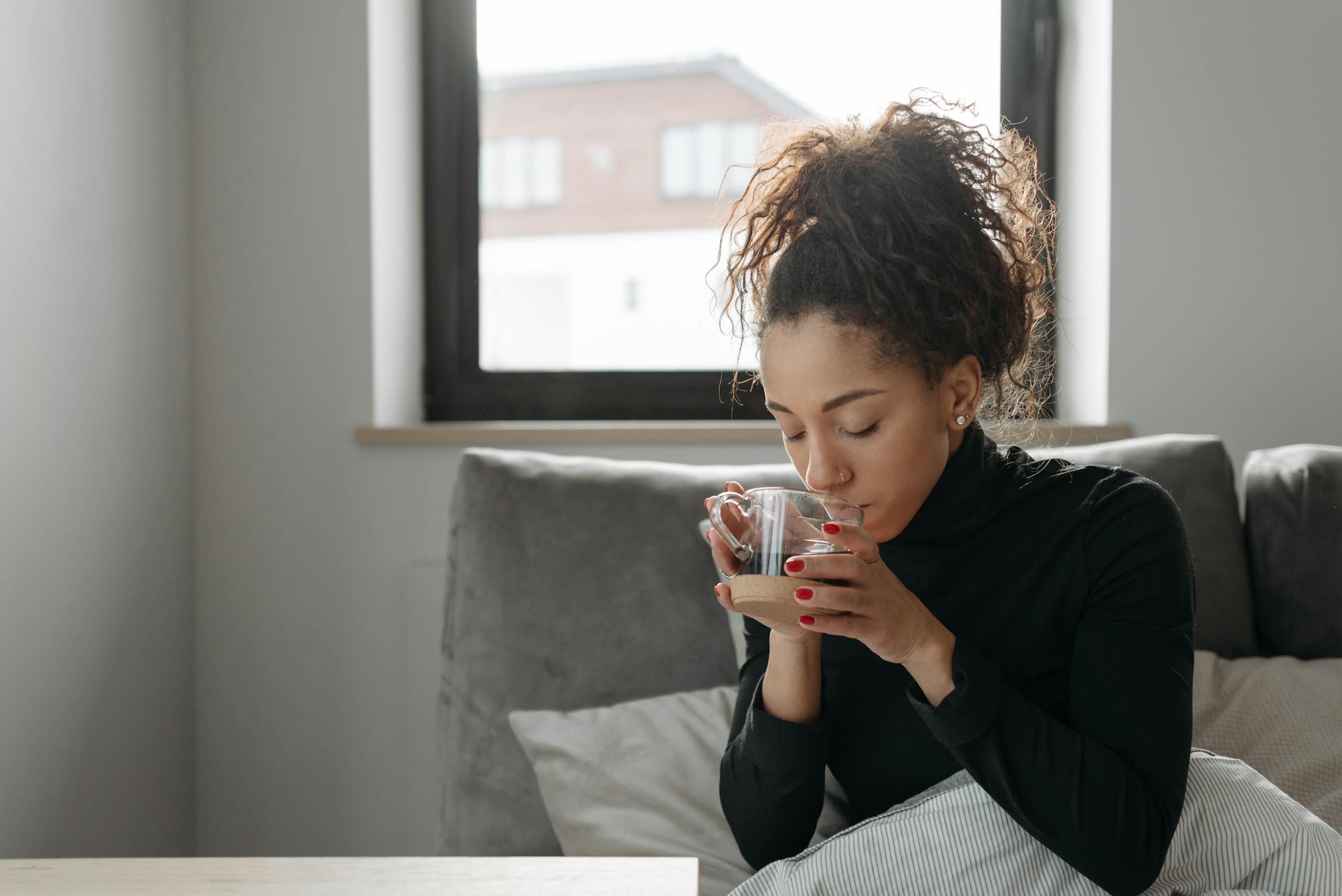 Young woman sipping tea indoors, creating a calming cozy atmosphere.