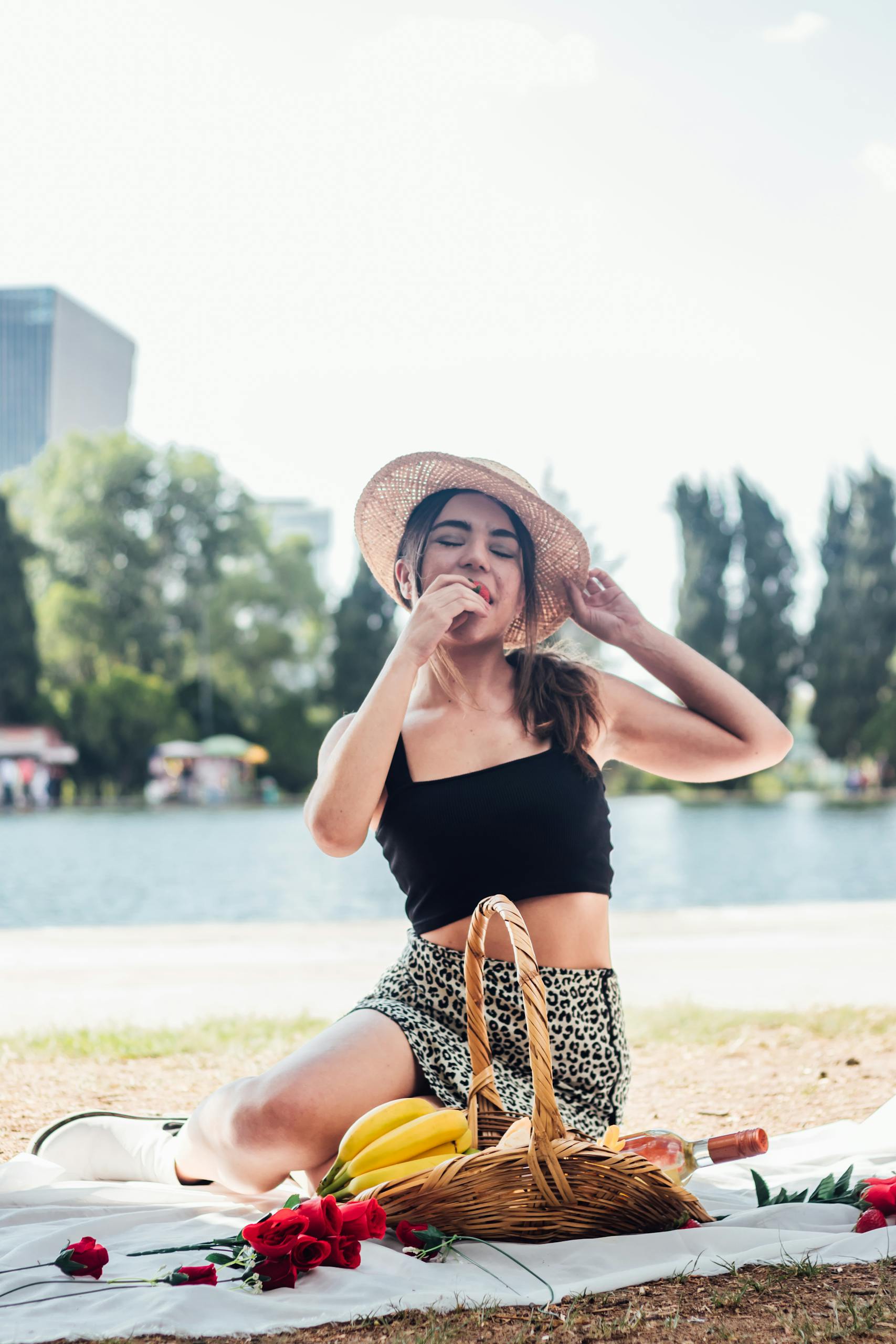 Young woman sitting on a picnic blanket by the lake, enjoying a sunny day outdoors.