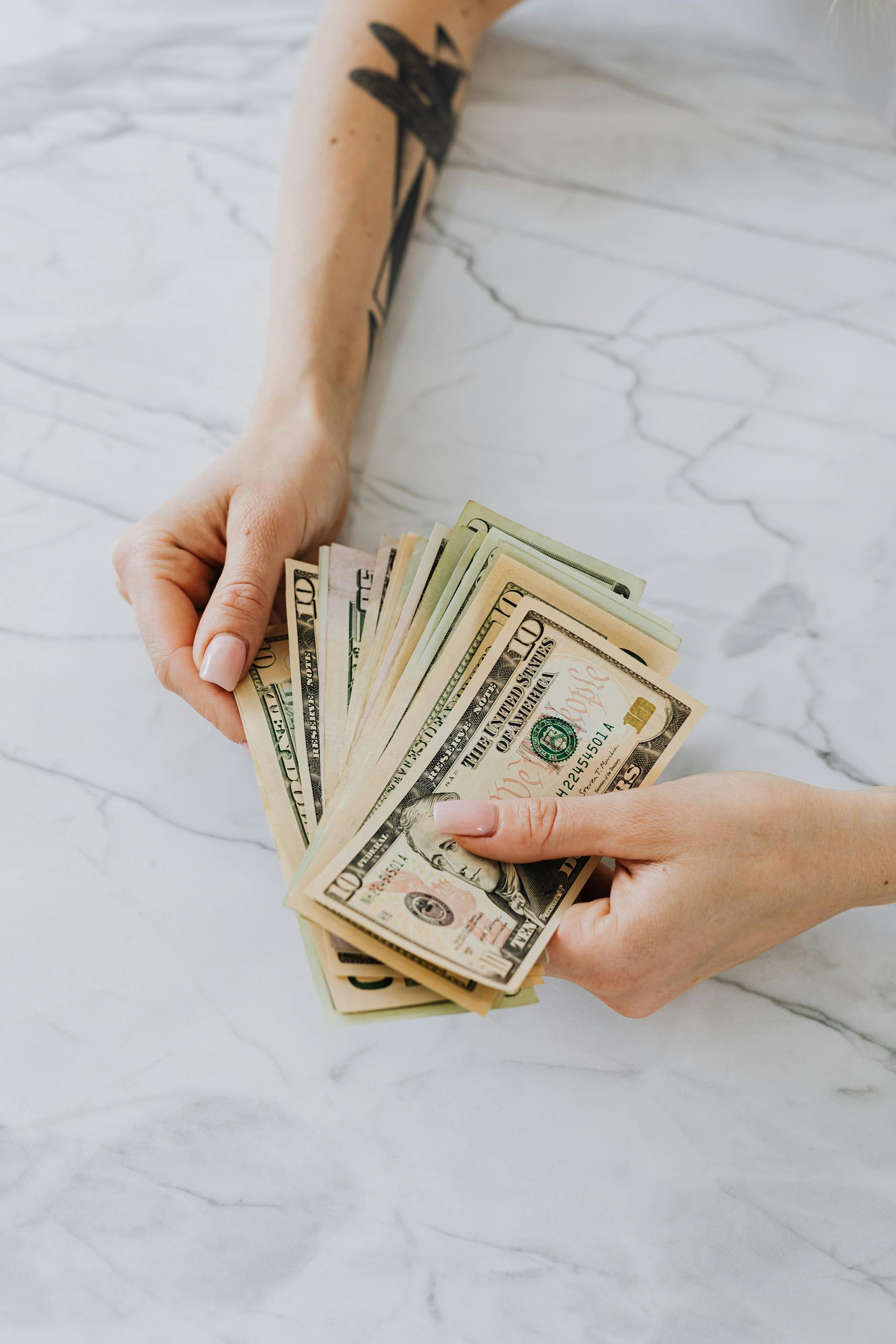 Hands holding a fan of US dollar bills on a marble table, symbolizing wealth and finance.