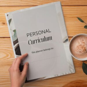 front page of the personal curriculum planner on a desk with a persons hand ready to open it