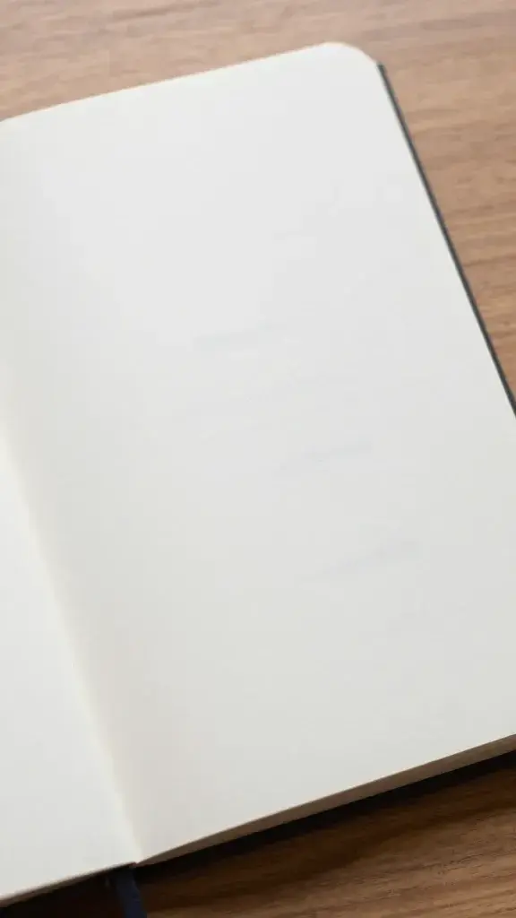 Closeup of an open journal with a single handwritten prompt visible, on a wooden desk