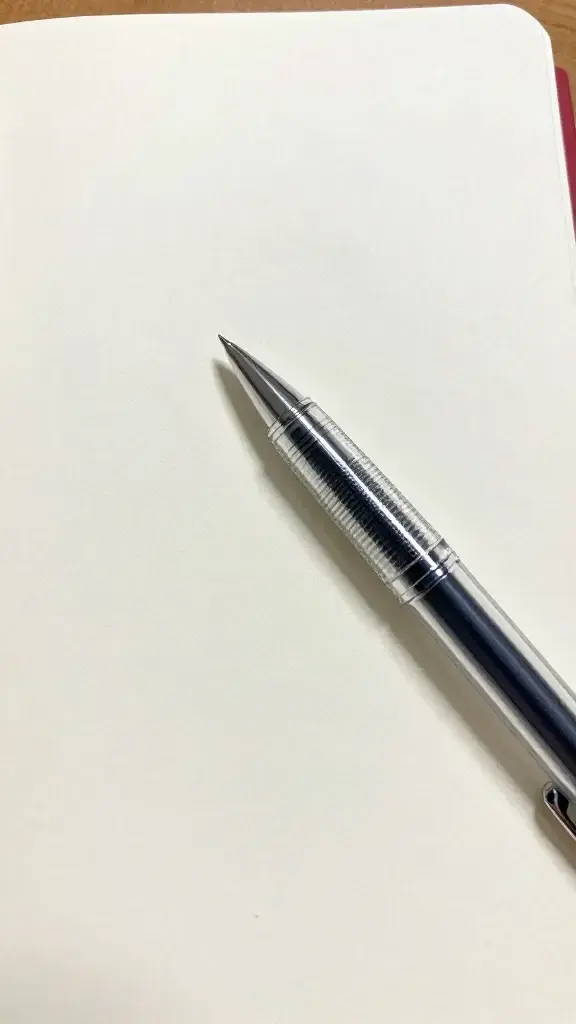closeup of a single crystal-clear pen poised over a blank journal page