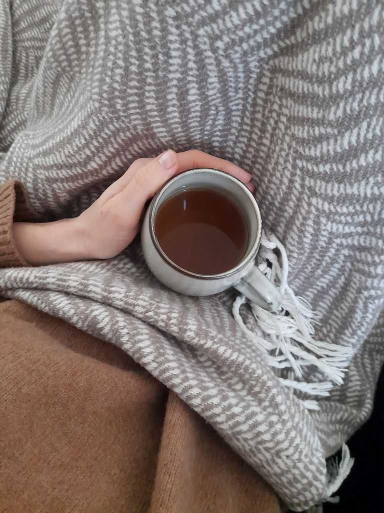 A comforting scene of a hand holding a tea cup, wrapped in a cozy blanket, perfect for a relaxing day.