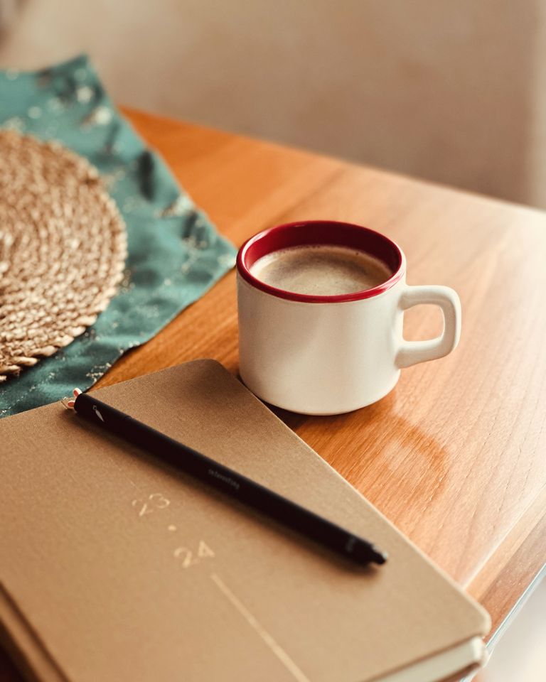 A cozy scene featuring a coffee mug, notebook, and pen on a wooden table, perfect for productivity.