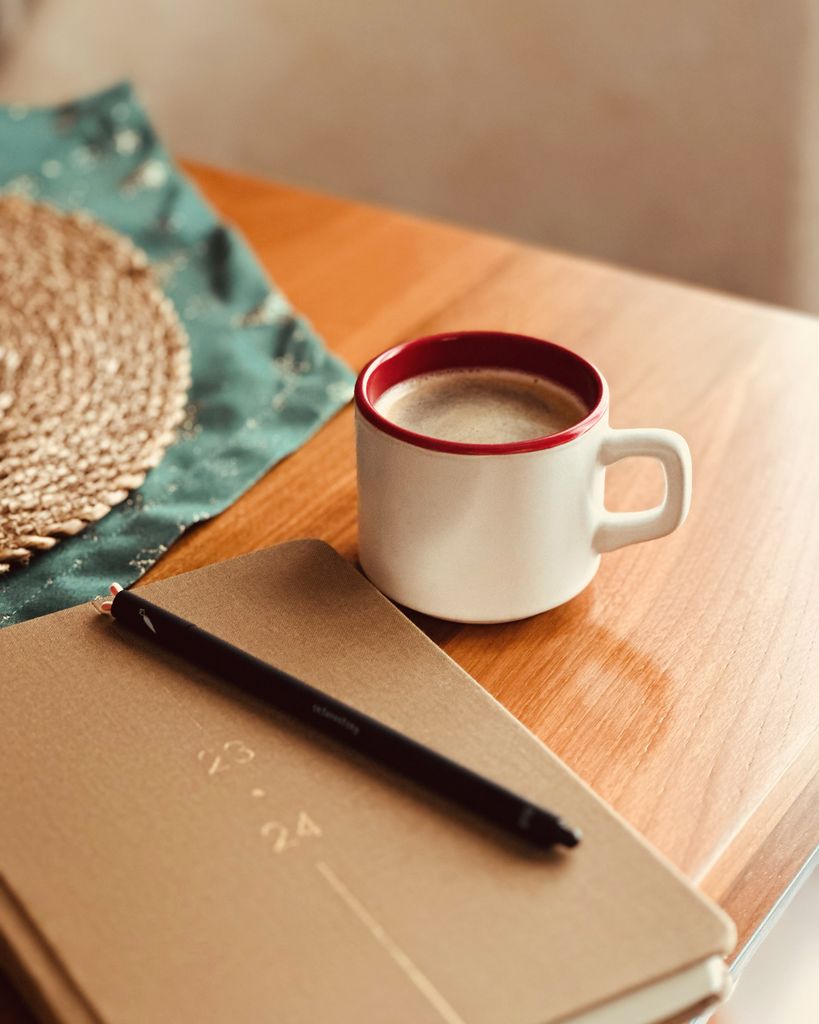 A cozy scene featuring a coffee mug, notebook, and pen on a wooden table, perfect for productivity. new years journal prompts