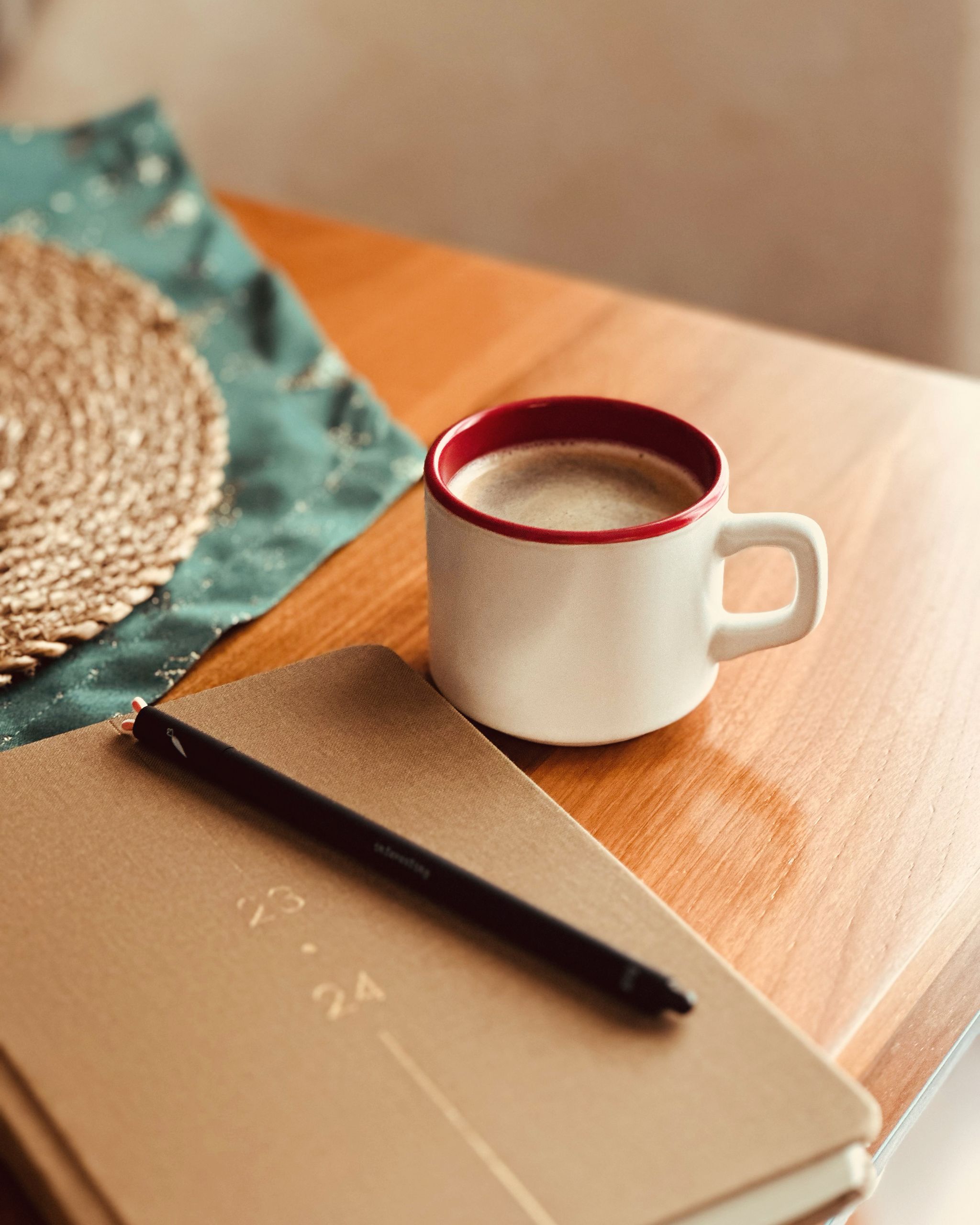 A cozy scene featuring a coffee mug, notebook, and pen on a wooden table, perfect for productivity.