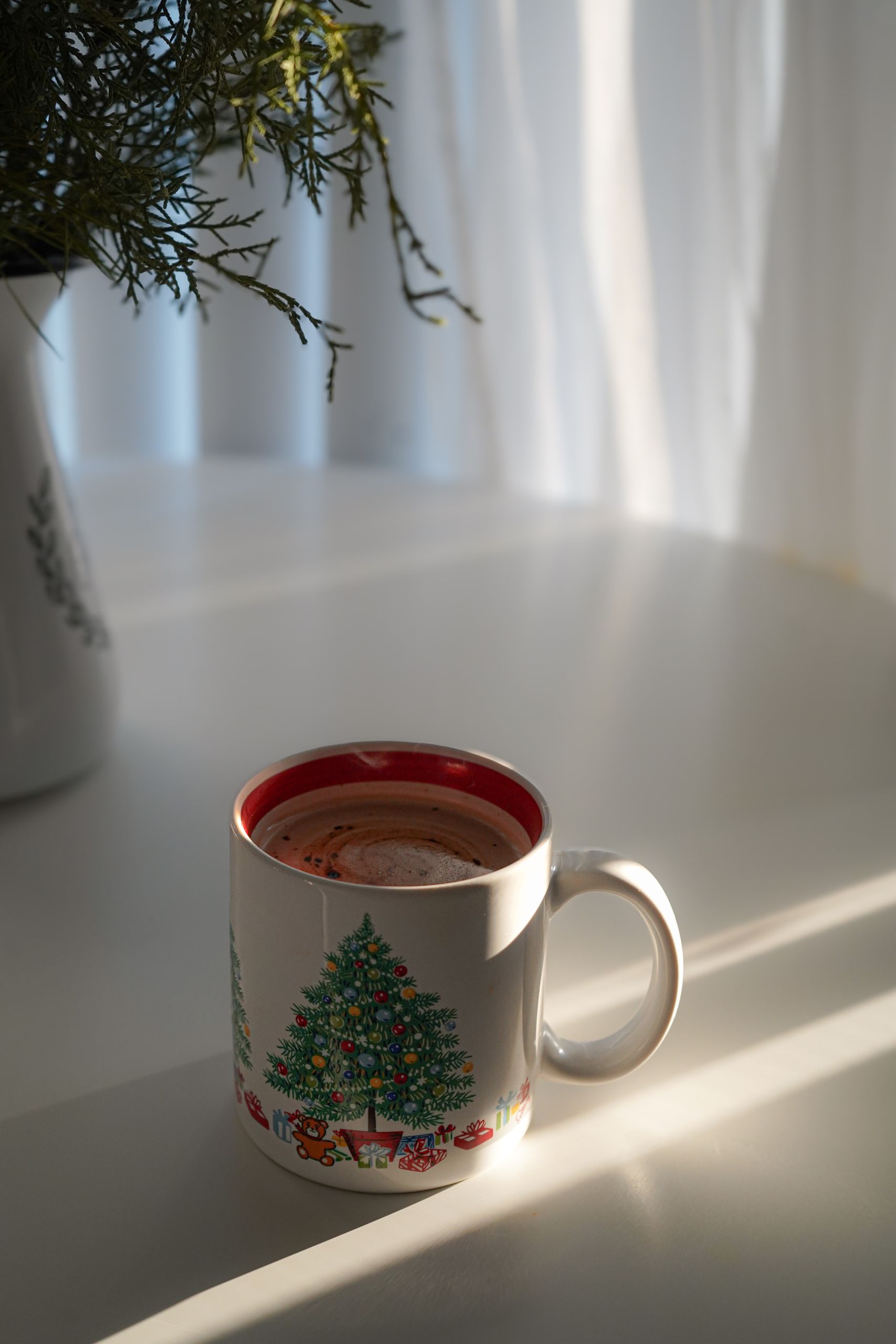 A festive Christmas mug filled with coffee in bright morning sunlight.