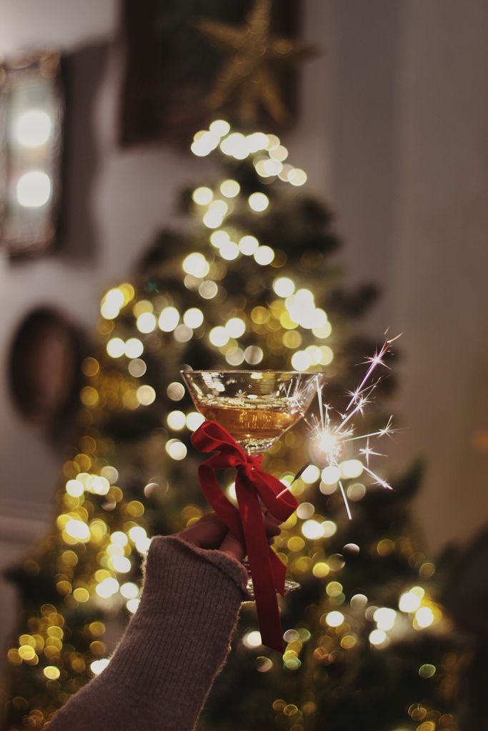 A festive moment with champagne and a sparkler in front of a Christmas tree with lights.