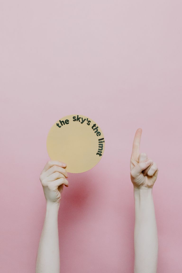 A hand holds a circular card with the phrase 'The sky's the limit' on a pink background.