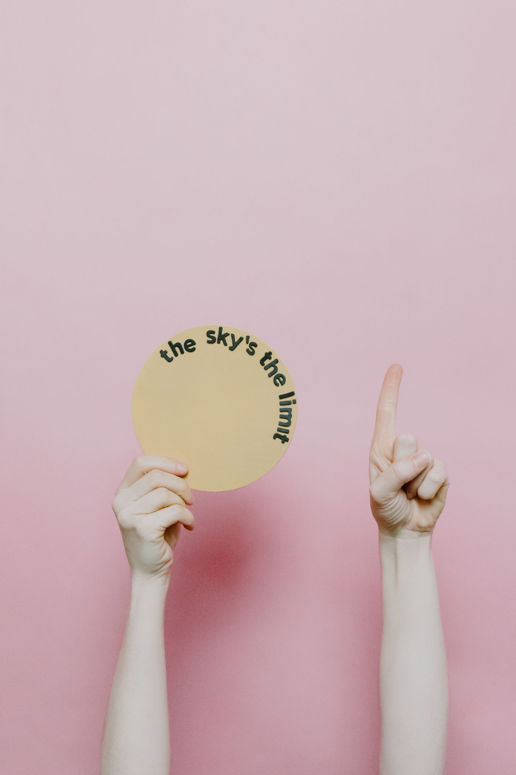 A hand holds a circular card with the phrase 'The sky's the limit' on a pink background.