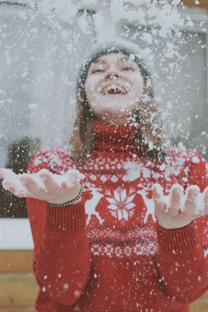 A happy woman in a festive red sweater playing with snow, capturing the essence of winter joy.