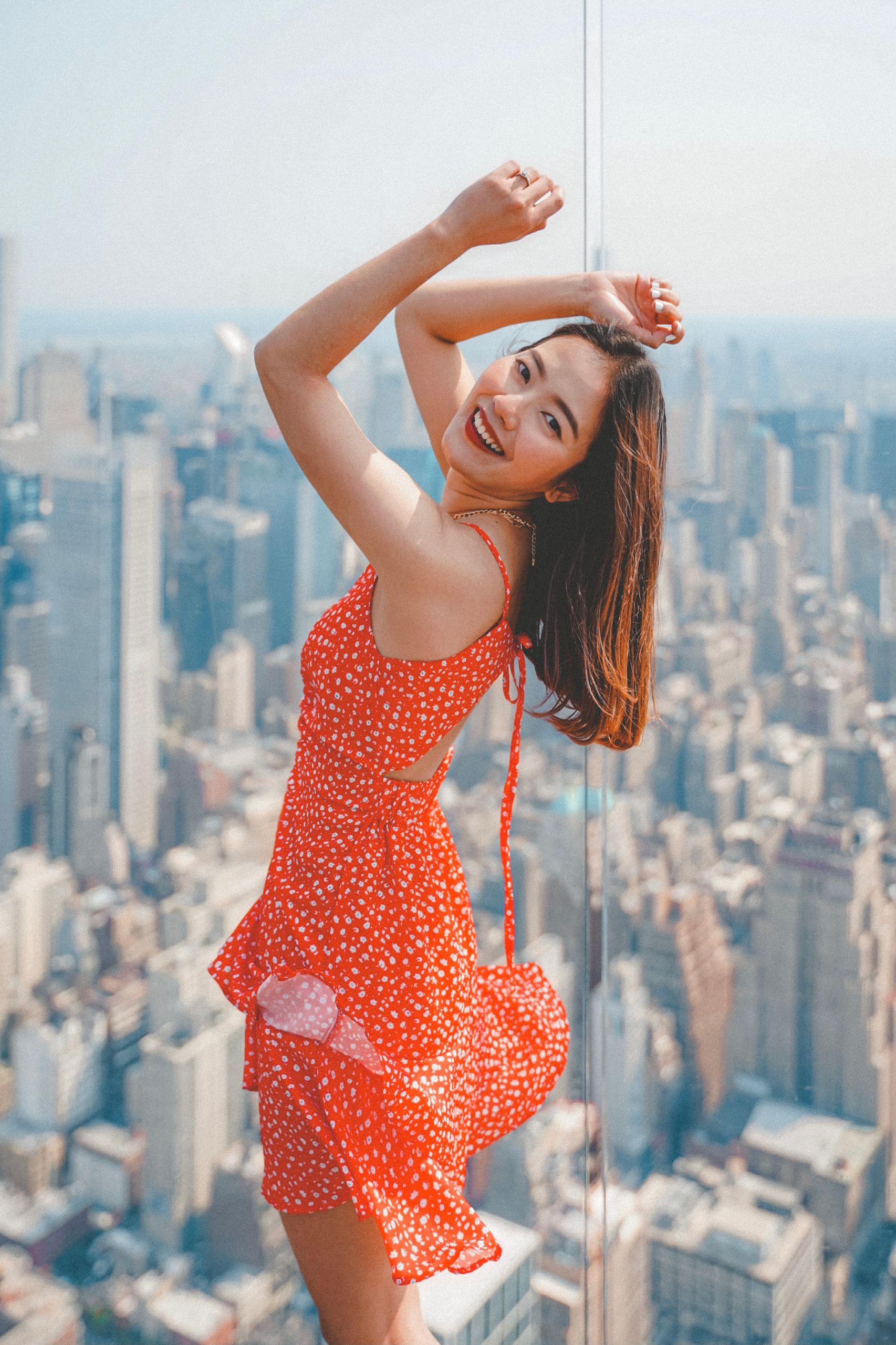 A joyful woman in a red dress poses with a cityscape backdrop, capturing the essence of New York City.