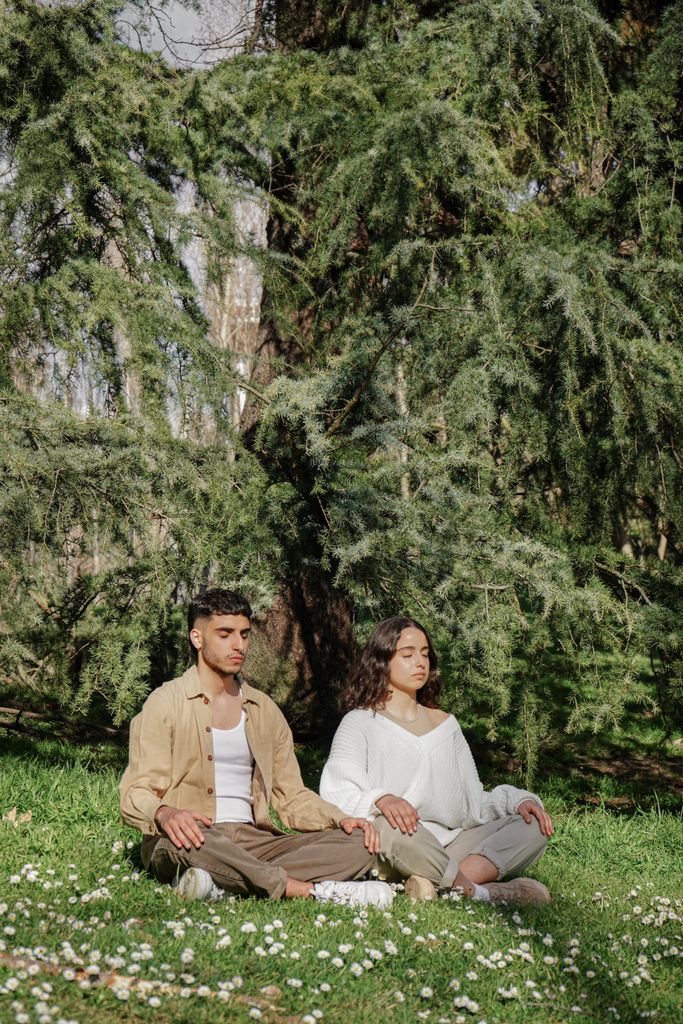 A man and woman meditating outdoors in a tranquil forest environment, embodying relaxation and mindfulness.