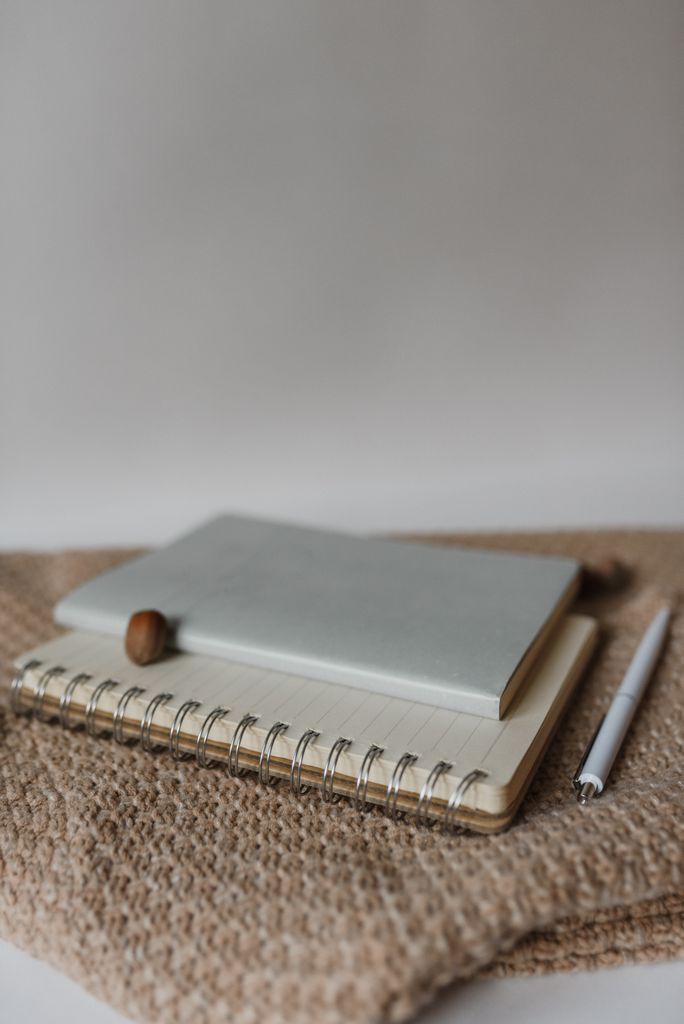 A minimalist composition featuring notebooks and a pen how to write gratitude journal on a woven surface, perfect for office or study themes.
