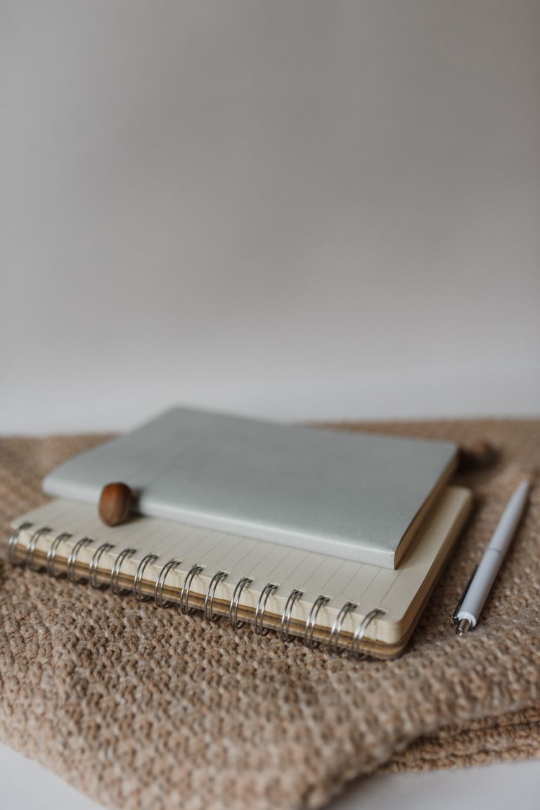 A minimalist composition featuring notebooks and a pen how to write gratitude journal on a woven surface, perfect for office or study themes.