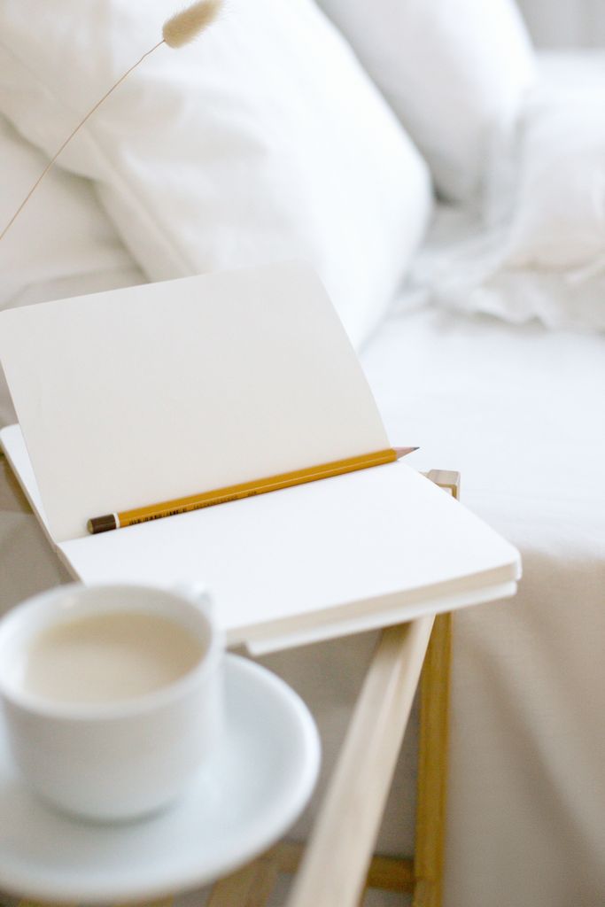 A minimalist home workspace featuring an open notebook and pencil with coffee on a wooden tray. how to start journaling step by step