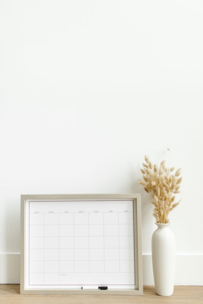 A minimalist setup featuring a framed calendar and decorative vase against a white background. 30 day self love challenge