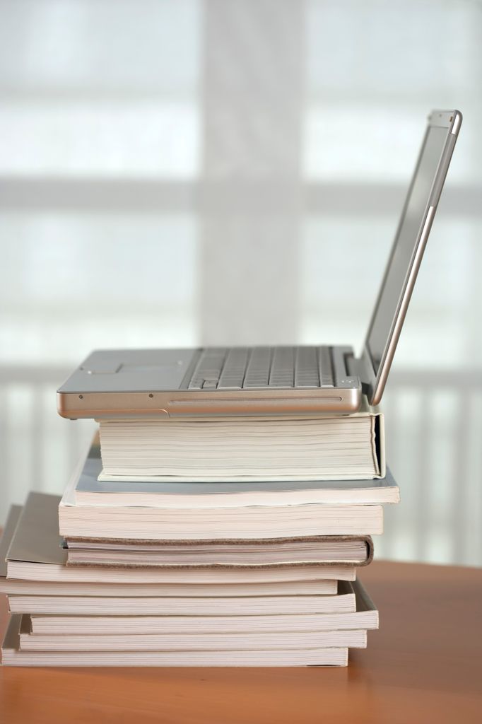 A modern laptop placed on a stack of books indoors, suggesting learning or work.