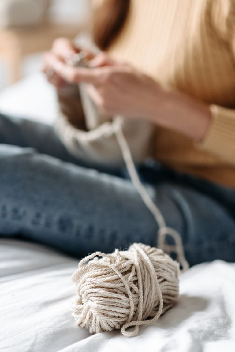 A person knitting indoors with a focus on natural yarn, capturing a cozy and warm atmosphere.