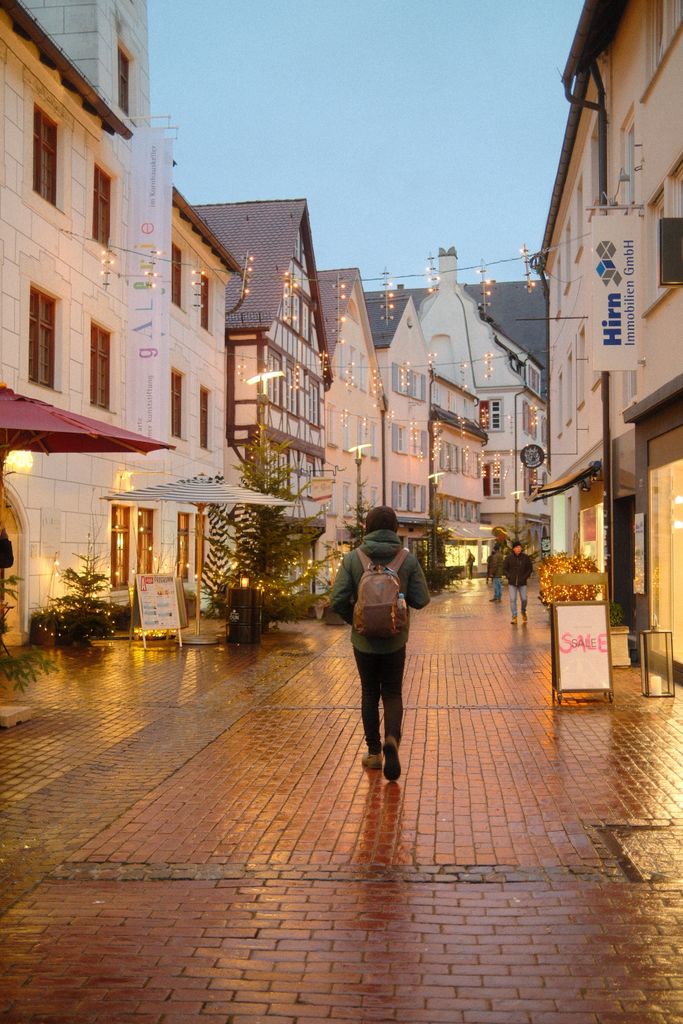 A person walking through the illuminated historic streets of Ulm, Germany during a festive evening.
