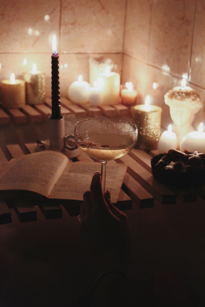 A serene setup of a bathtub with candles, champagne, and a book, evoking a sense of relaxation. self care night checklist